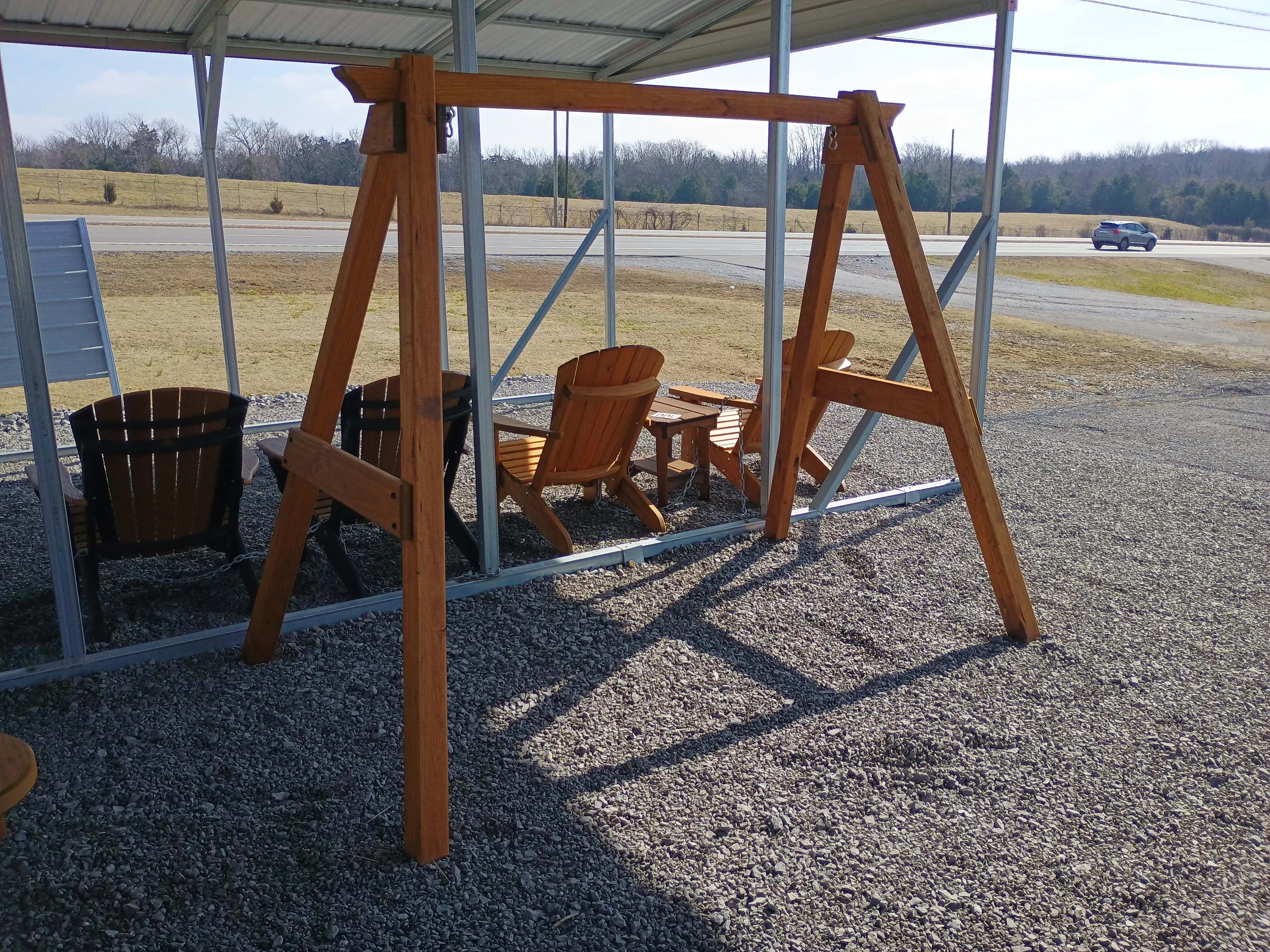 a wood a-frame structure standing in the gravel. There are chairs sitting behind it