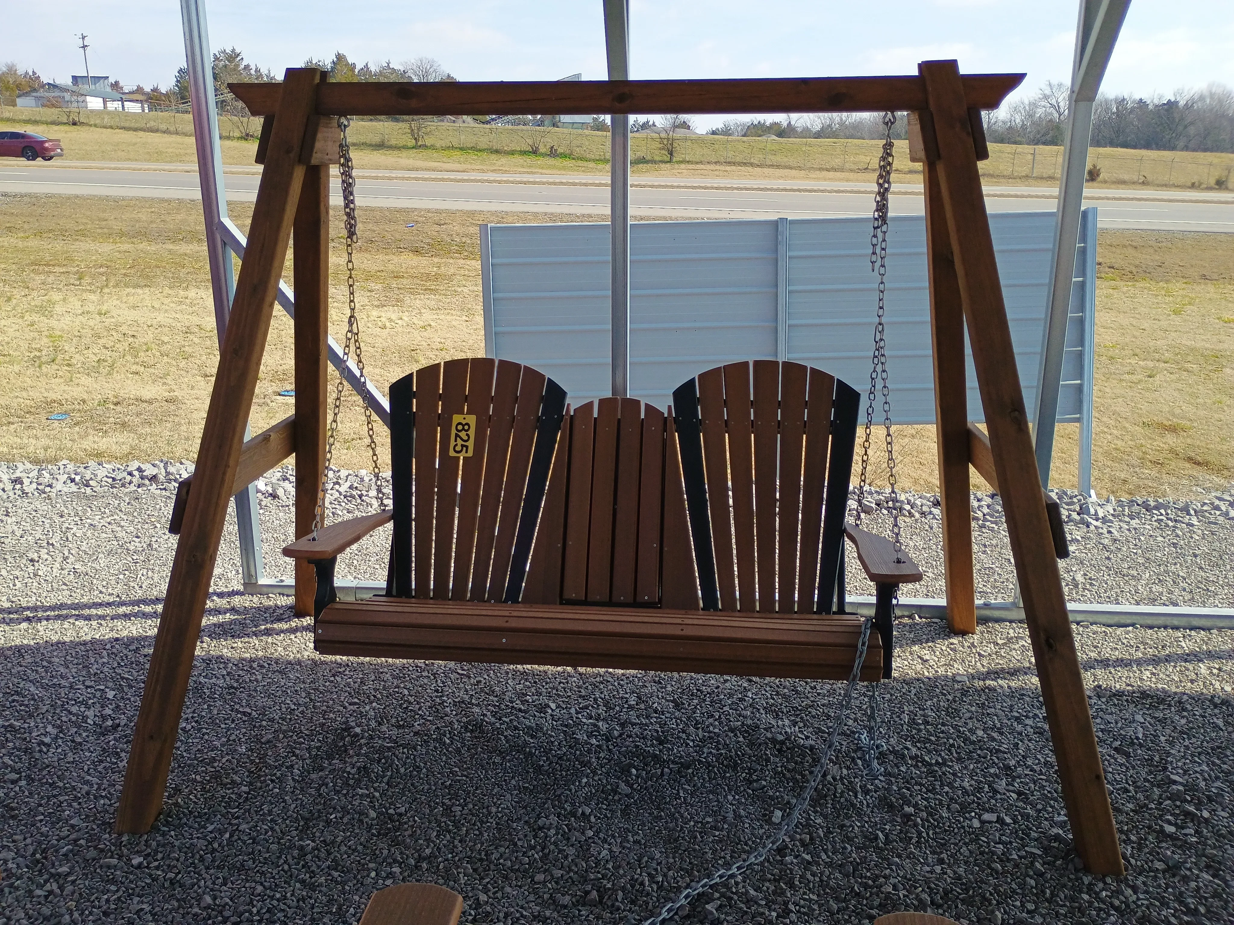 a wooden a-frame structure holding up a bench in the gravel. It is under a carport