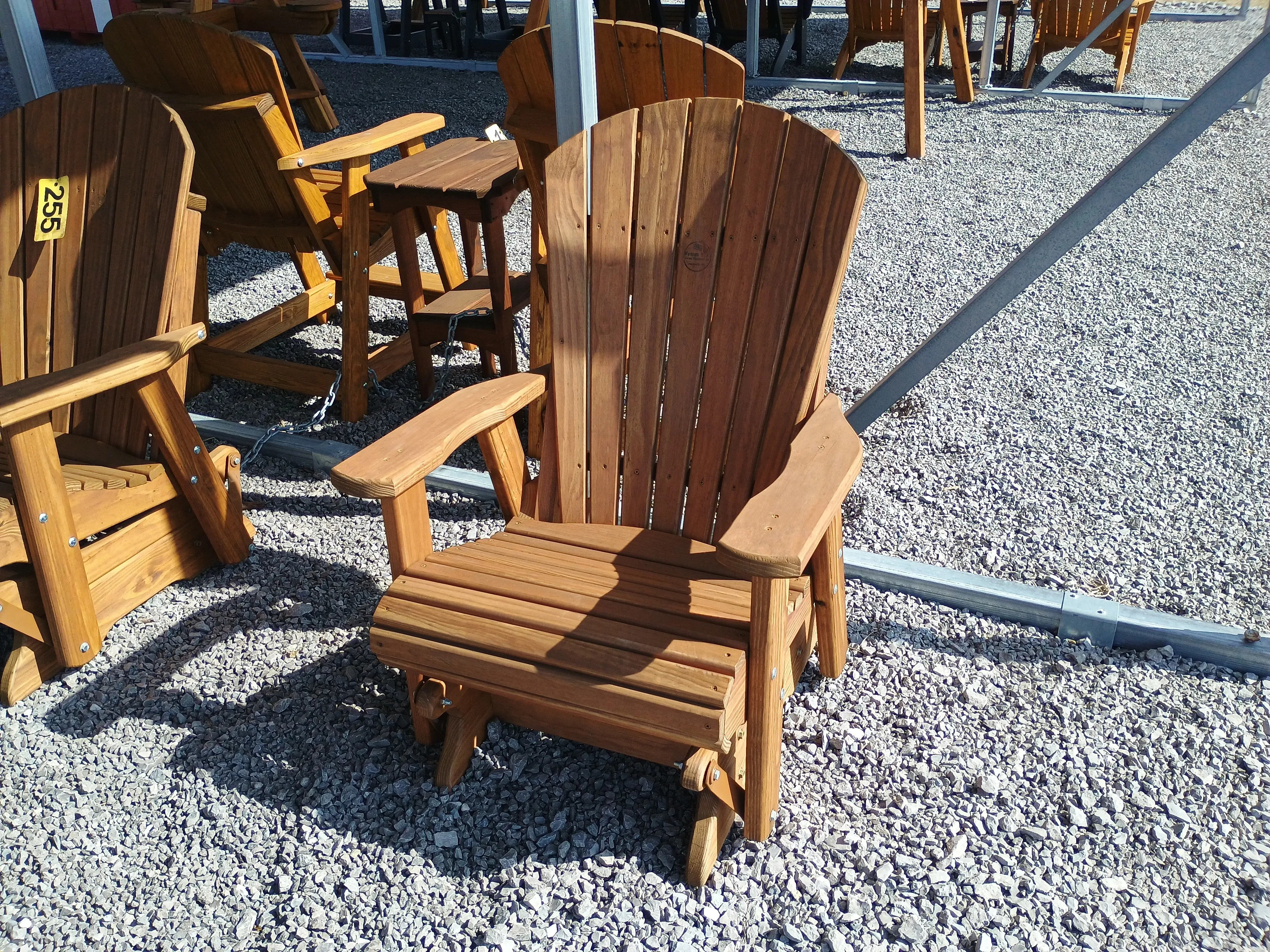 a wood stained and sealed chair that glides back and forth sitting under a carport in the gravel.