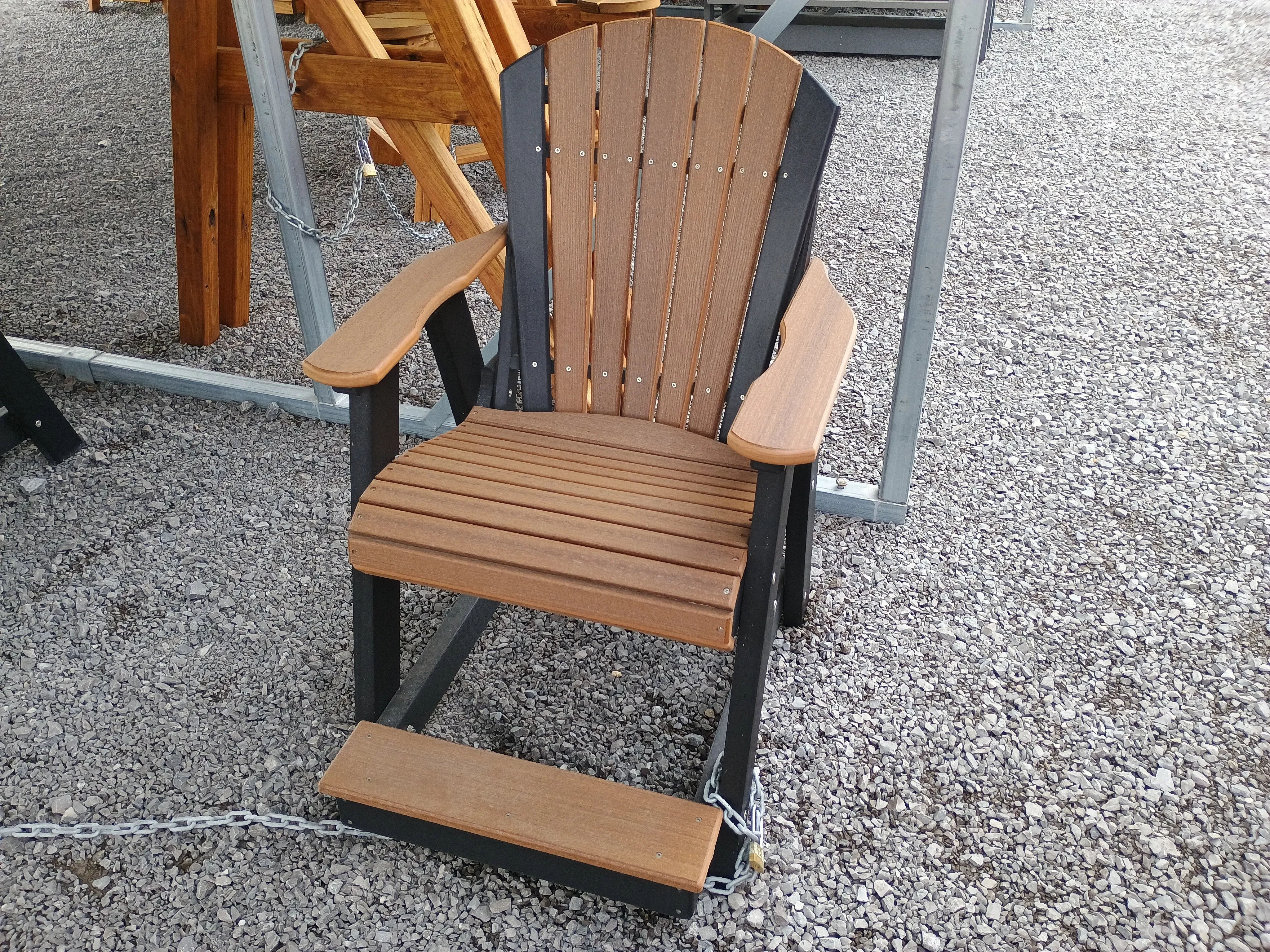 a chair sitting in the gravel under a carport. It is brown with black accents. It is chained up to other furniture