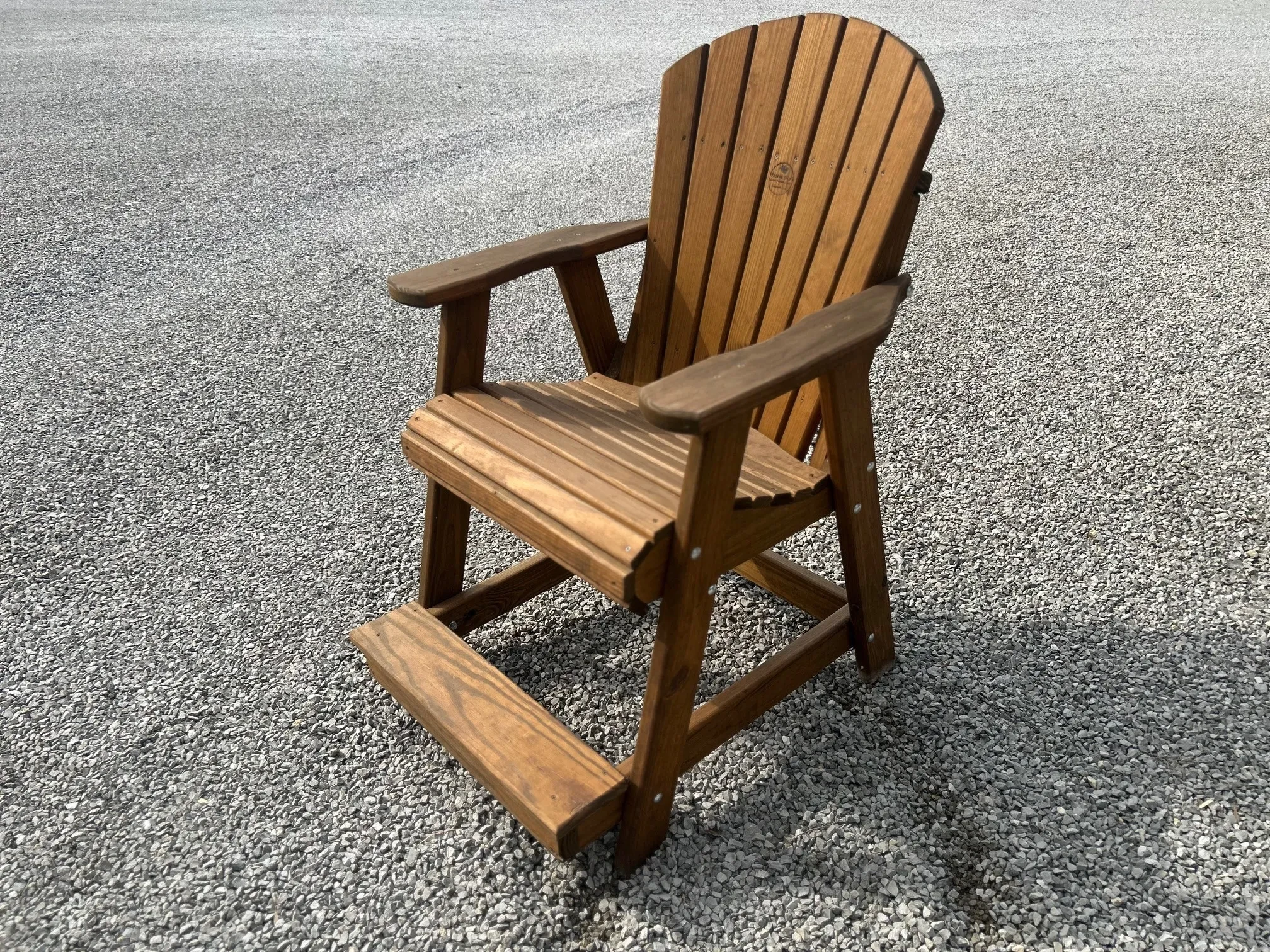 a wood stained and sealed chair sitting in the gravel. It has arm and footrests