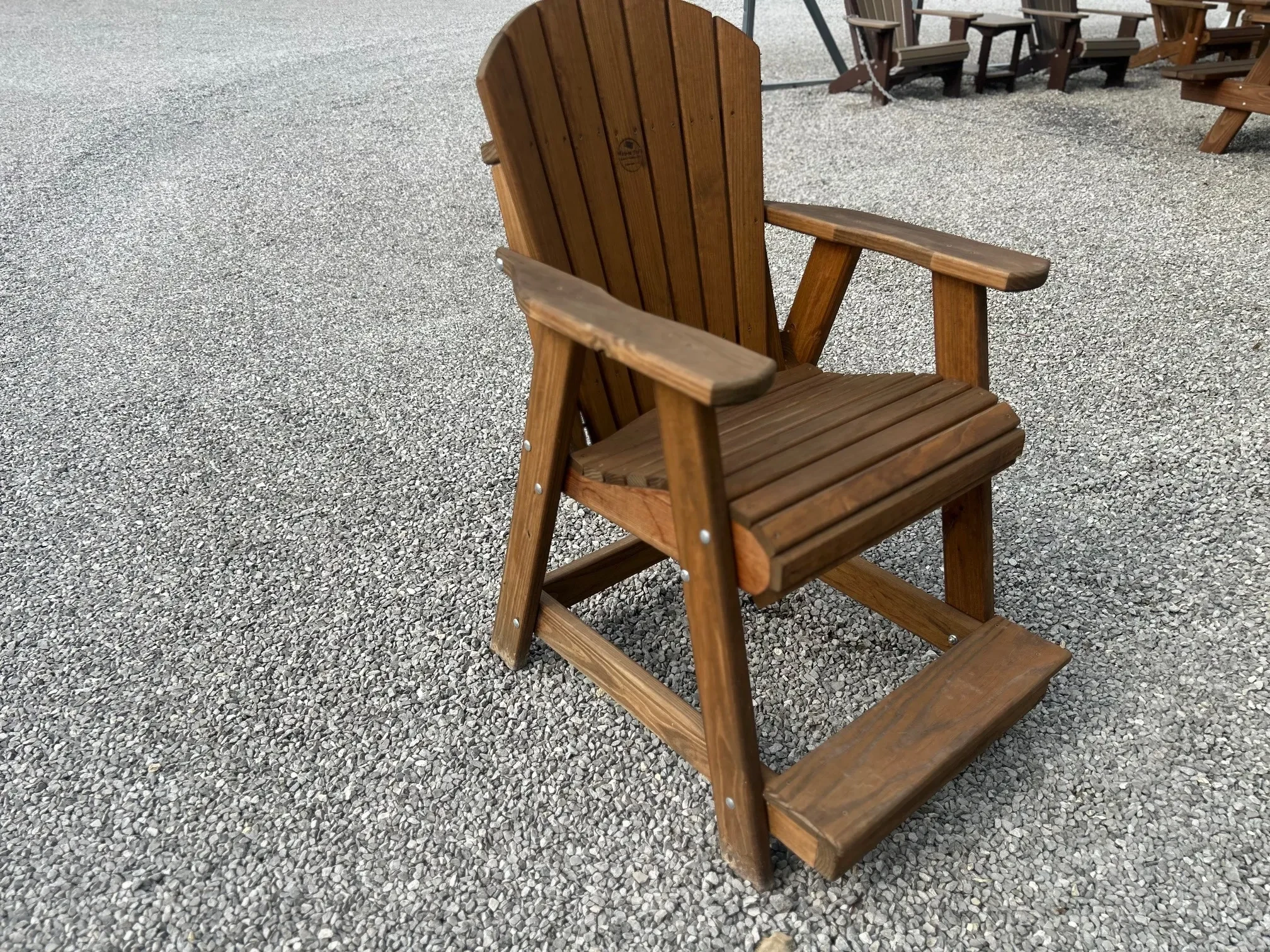 a chair sitting in the gravel. It has armrests and footrests and is nicely stained and sealed