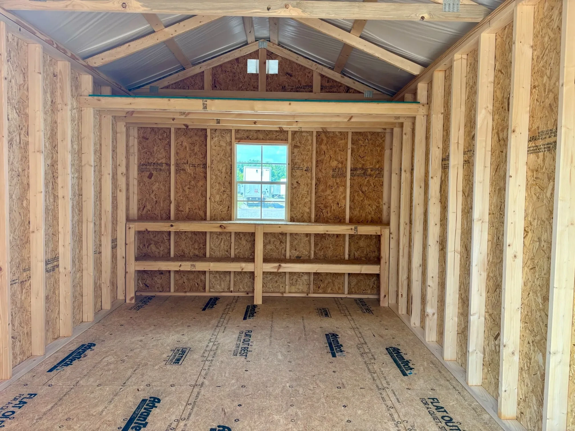 The inside of a wood shed showing double shelves, a window, and a loft on the back wall.