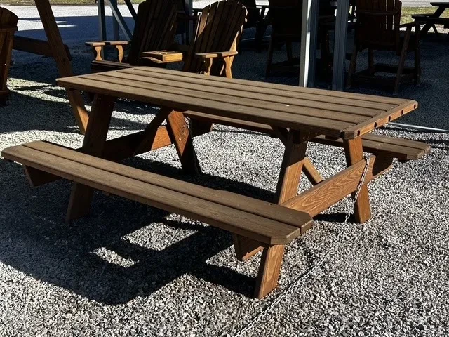 a wood stained and sealed picnic bench sitting in the gravel. It is chained up to other furniture
