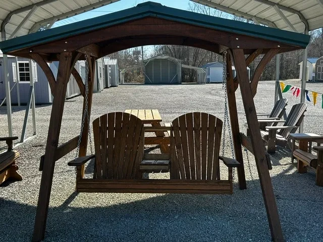 a wooden swing cover holding up a wooden bench. It is sitting in the gravel and there is other furniture around