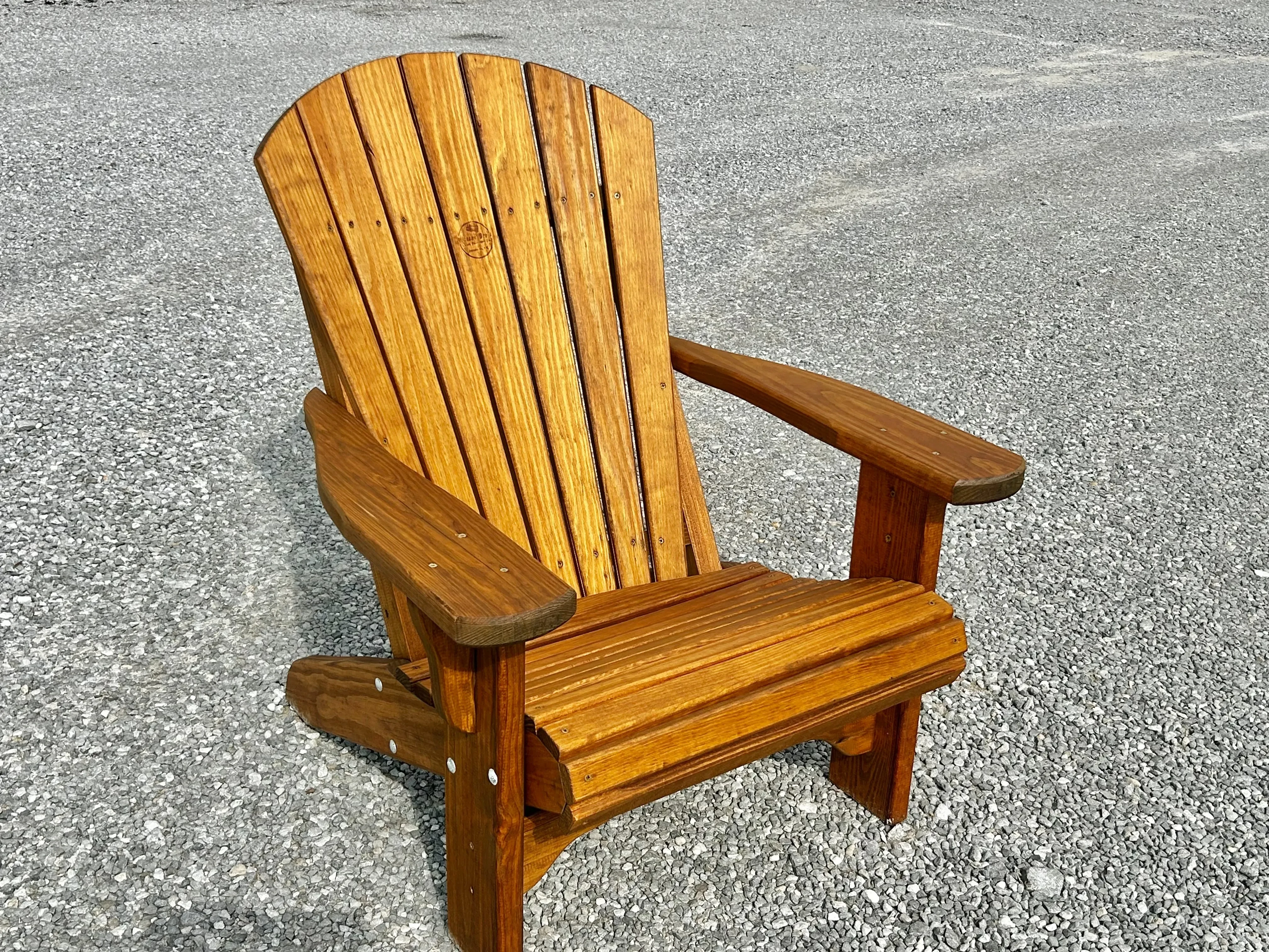 a wood chair sitting in the gravel. It is nicely stained and sealed.