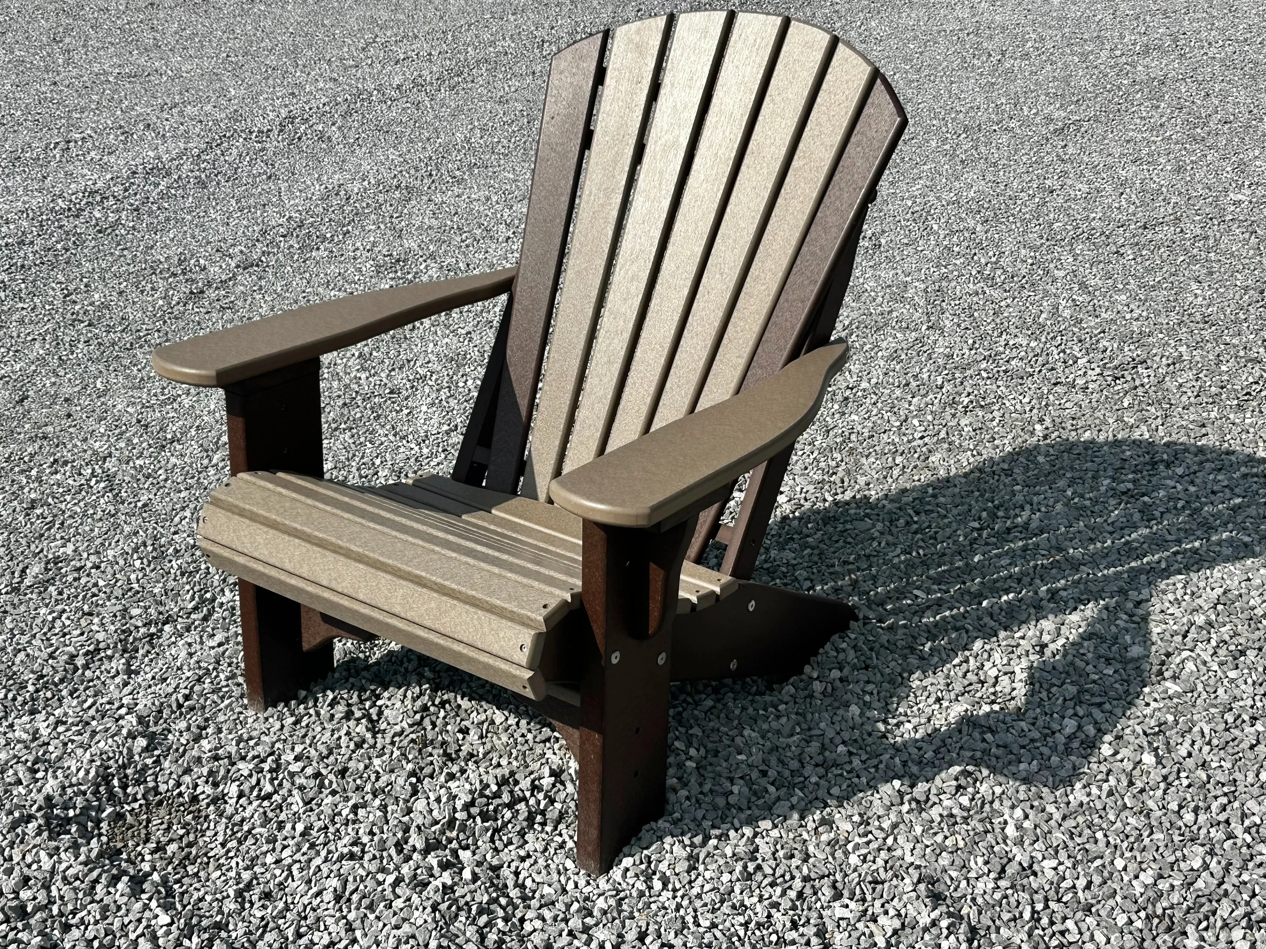 a chair sitting in the gravel with a shadow behind it. It is made out of a polywood material to last a long time