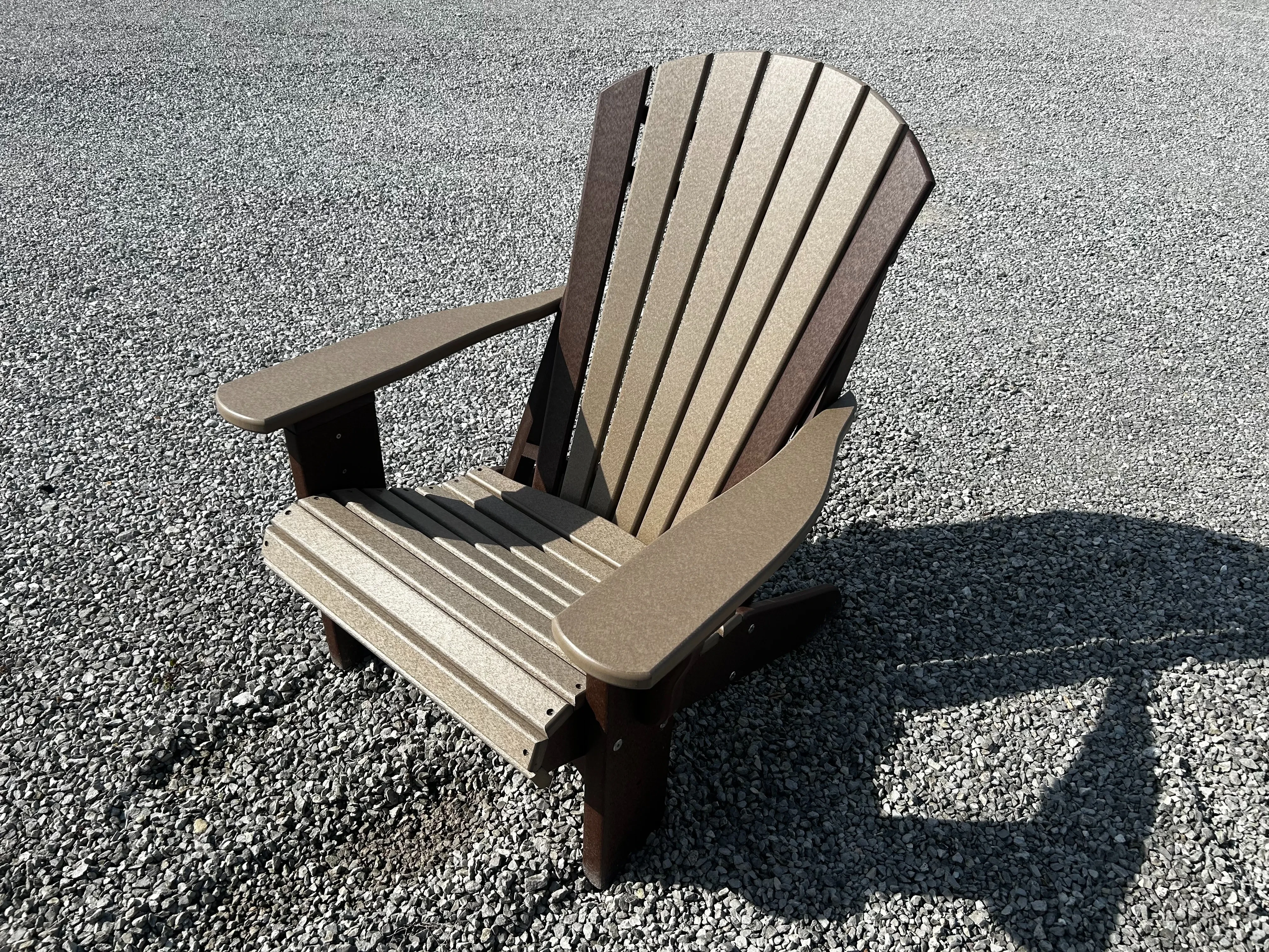 a two toned polywood chair sitting in the gravel with a shadow behind it. It has armrests