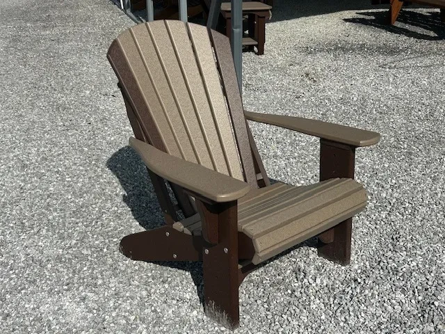 a chair made out of polywood sitting in the gravel. It's shadow is behind it. It is a light gray color with brown accents
