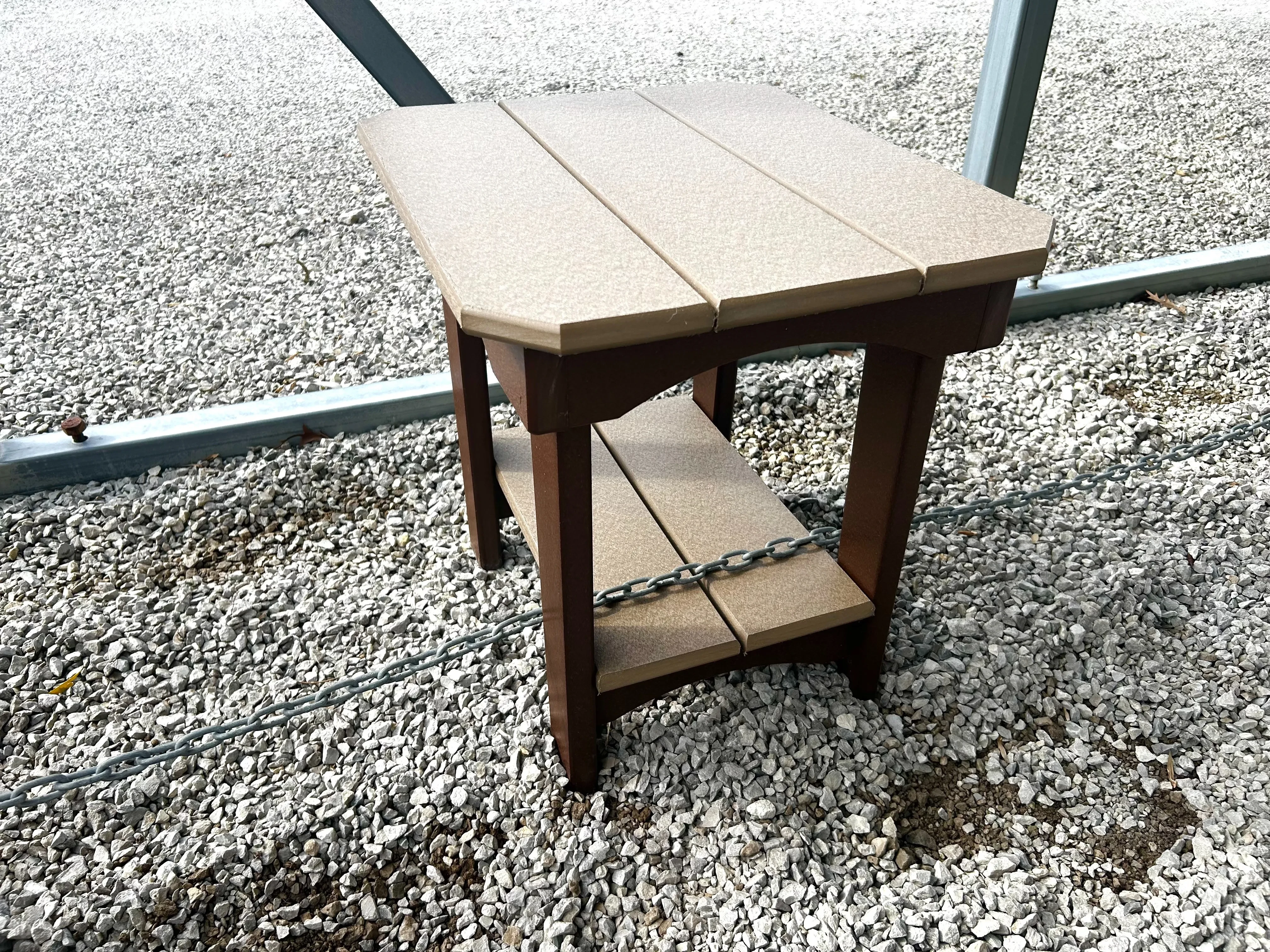a two tone colored table with a tabletop and a smaller tabletop towards the legs. It is sitting in the gravel