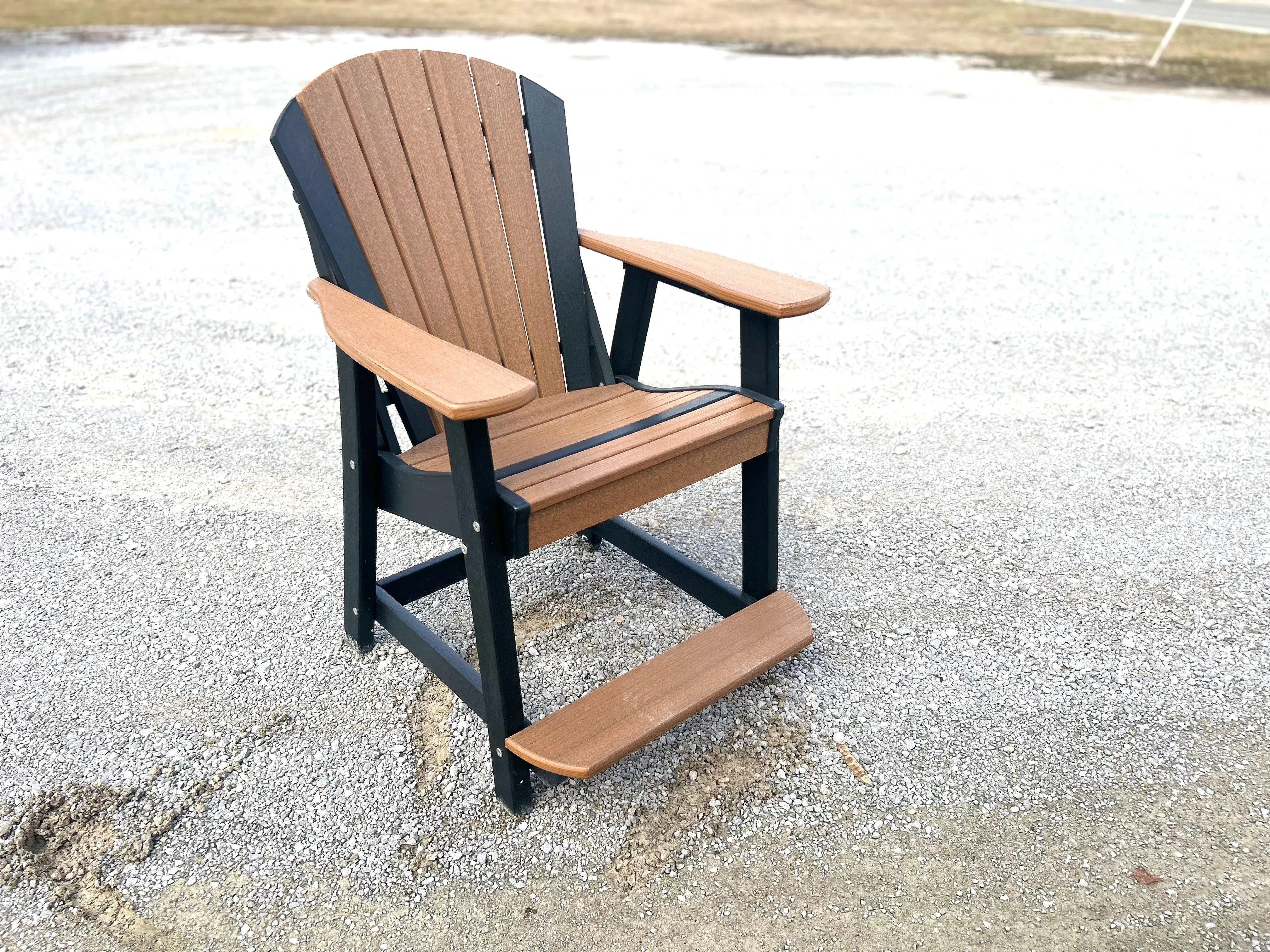 a chair sitting in the gravel. It is brown with blakc accents. It has arm rests and foot rests
