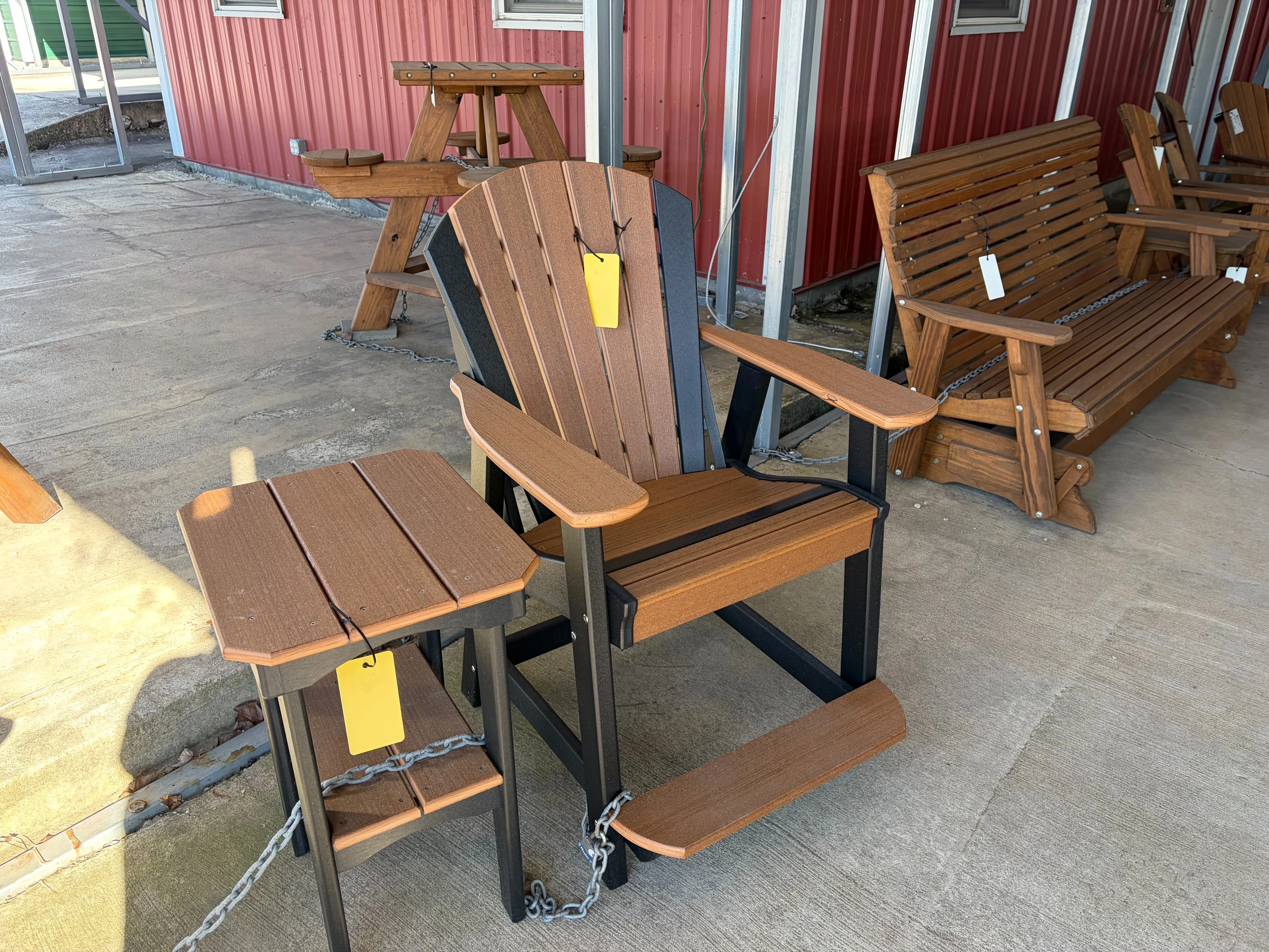 a polywood chair that is a weathered wood color with black accent colors, it's next to a polywood end table