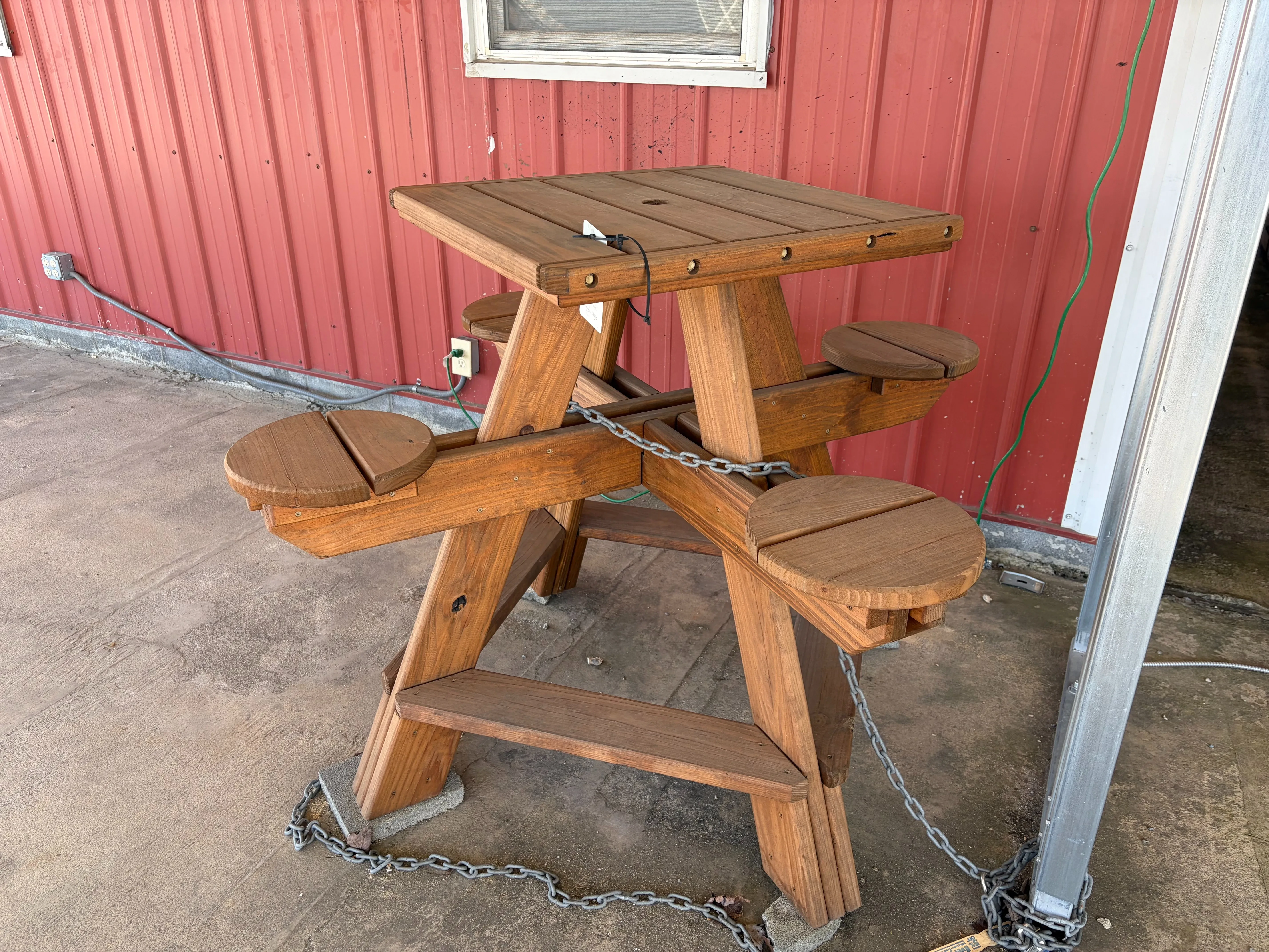 a table with four circular seats attached and the tabletop is square. It is chained up to a metal pole