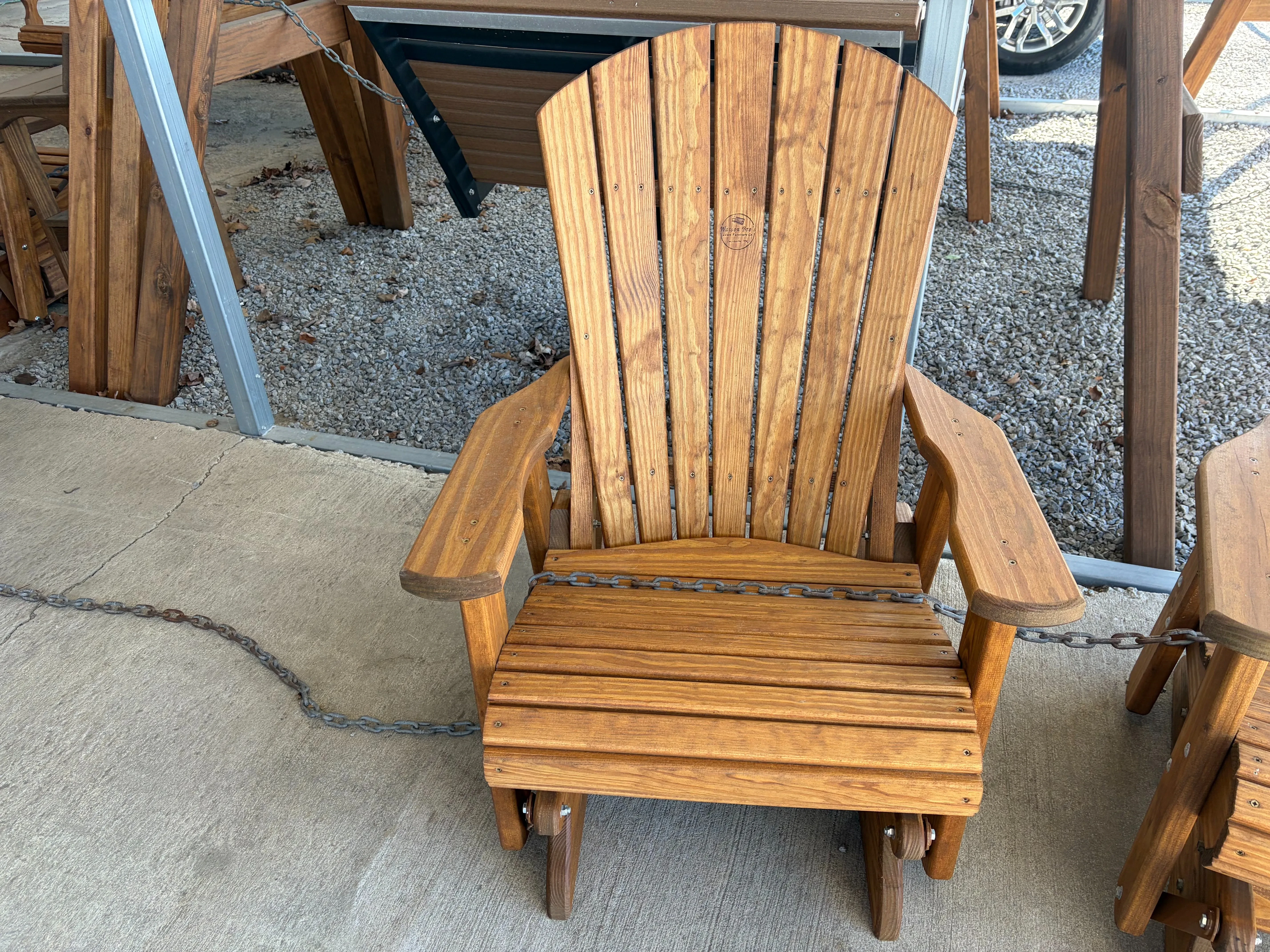 a wood chair sitting on concrete. It can glide back and forth. It is chained up to other furniture nearby