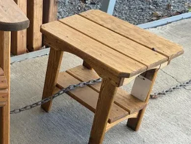 a nicely stained and sealed wood end table standing on the concrete. It has a two tabletops, one on top and one by the legs