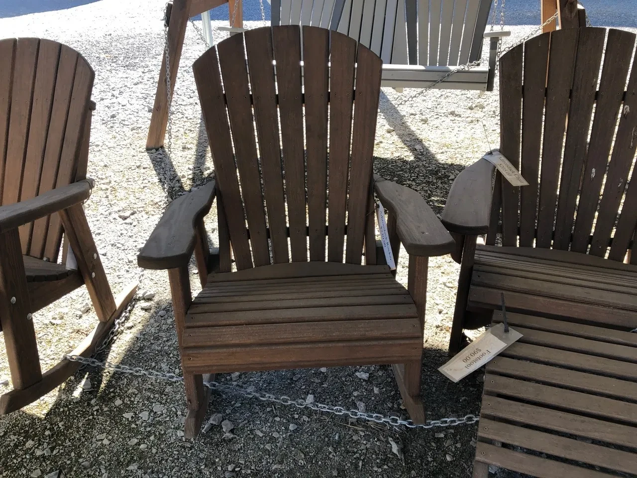 a wood rocking chair that has been stained and sealed sitting in the shade. It has armrests. It is chained up