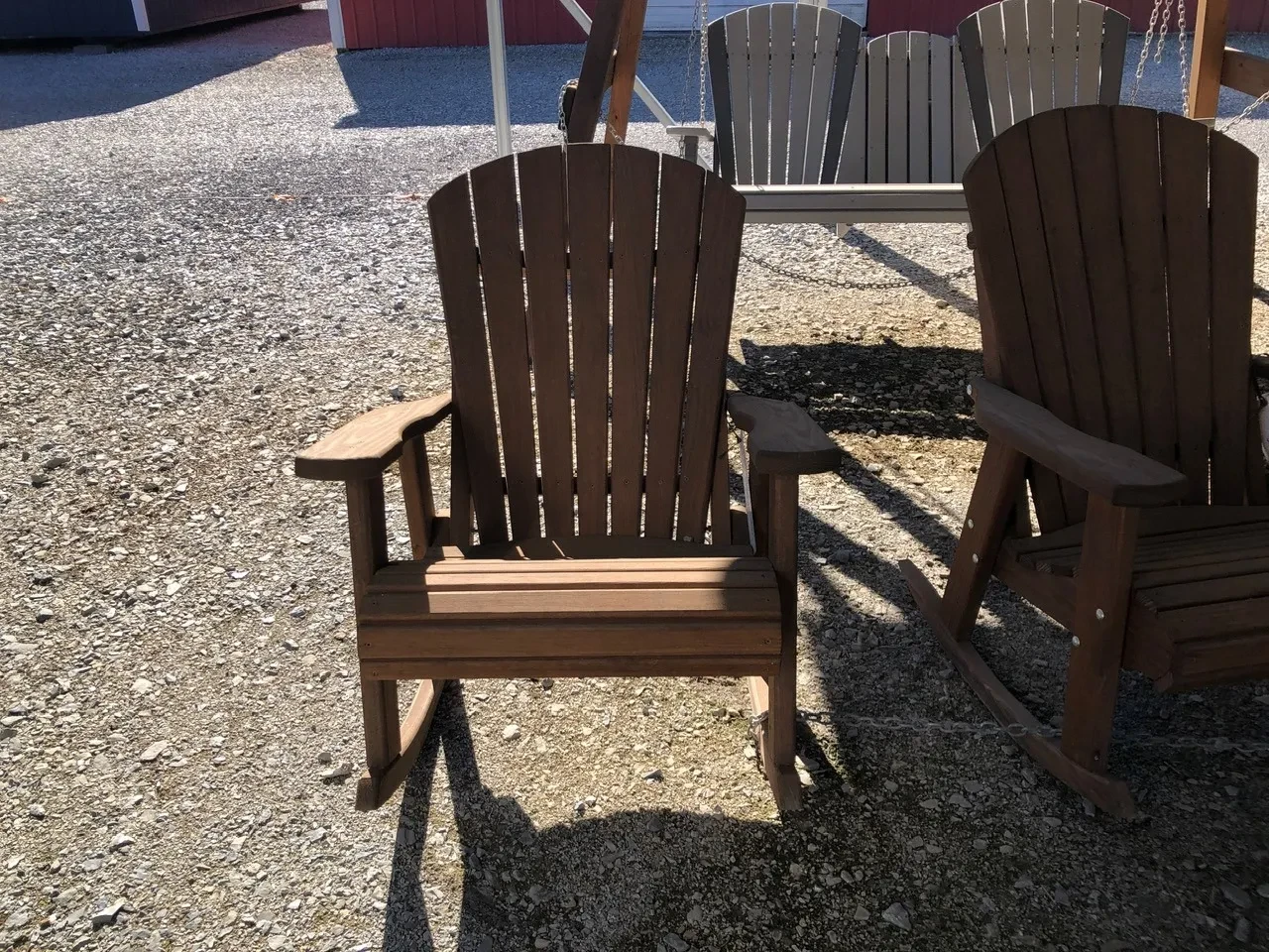 a wood stained and sealed rocking chair sitting in the shade, it is chained up to a chair next to it.