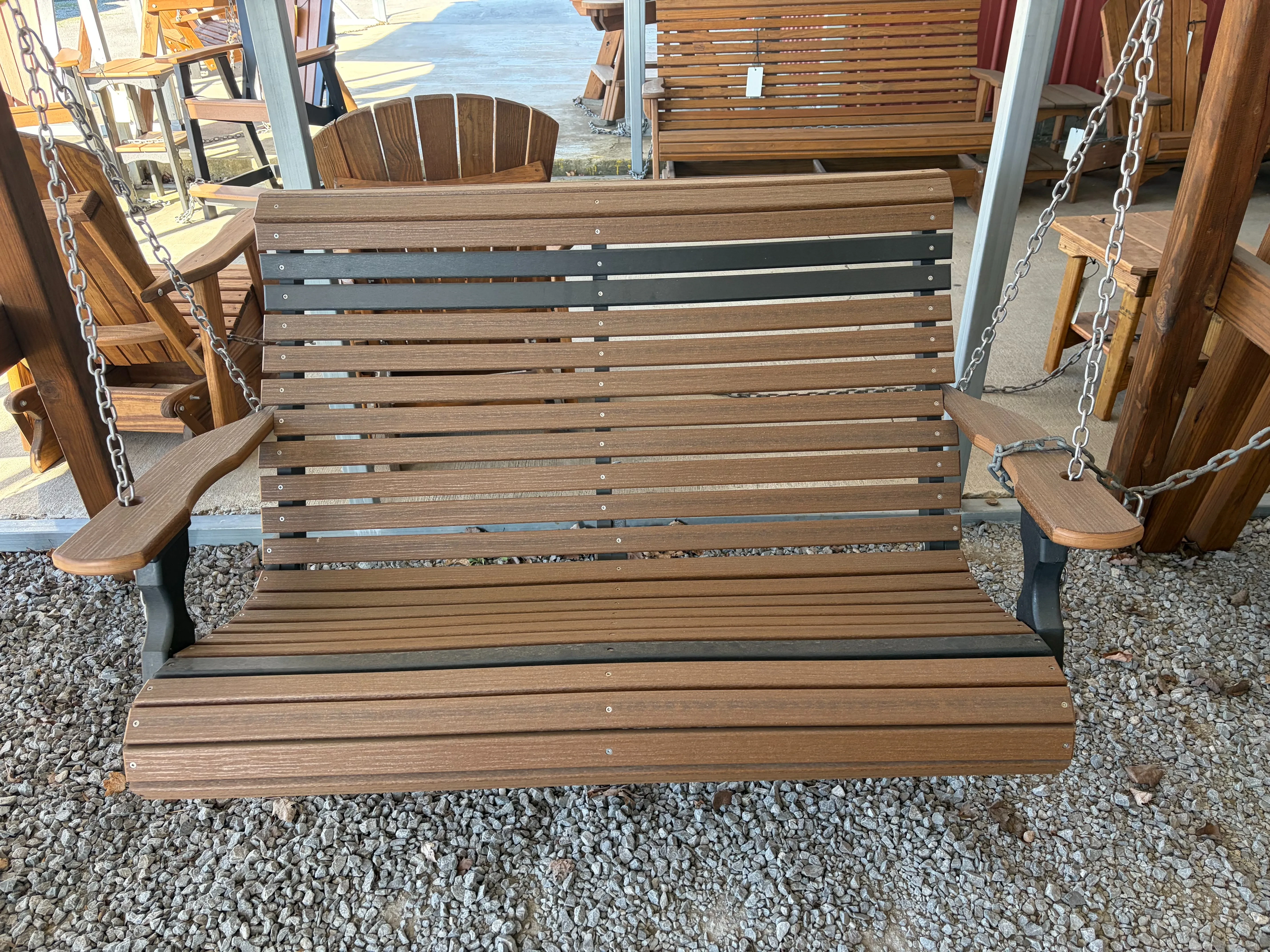 a brown bench swing with black accents. It is held up by an a-frame structure, hovering over some gravel.