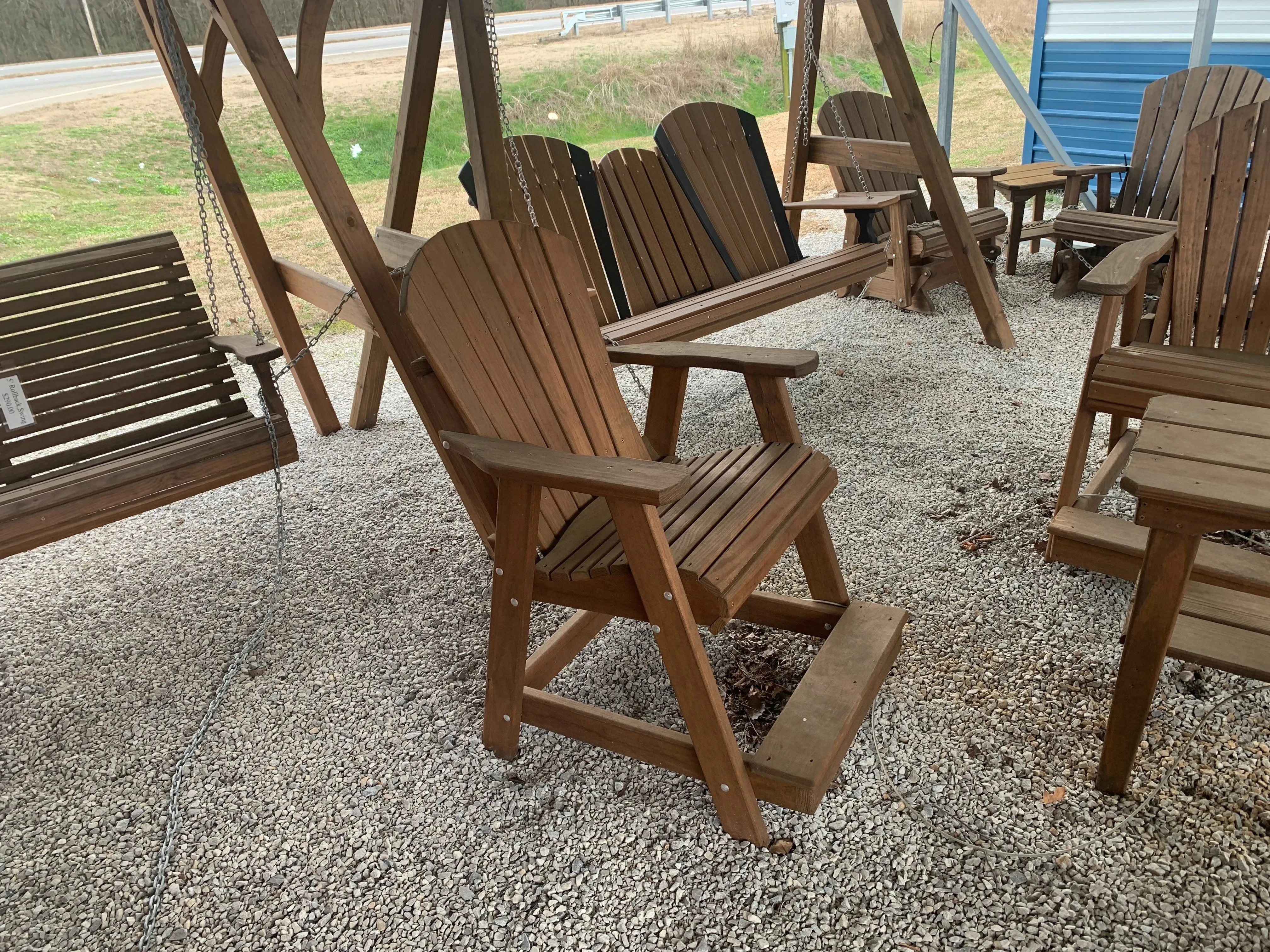 a wood chair sitting in the gravel next to other furniture. It is stained and sealed. It has armrests and footrests