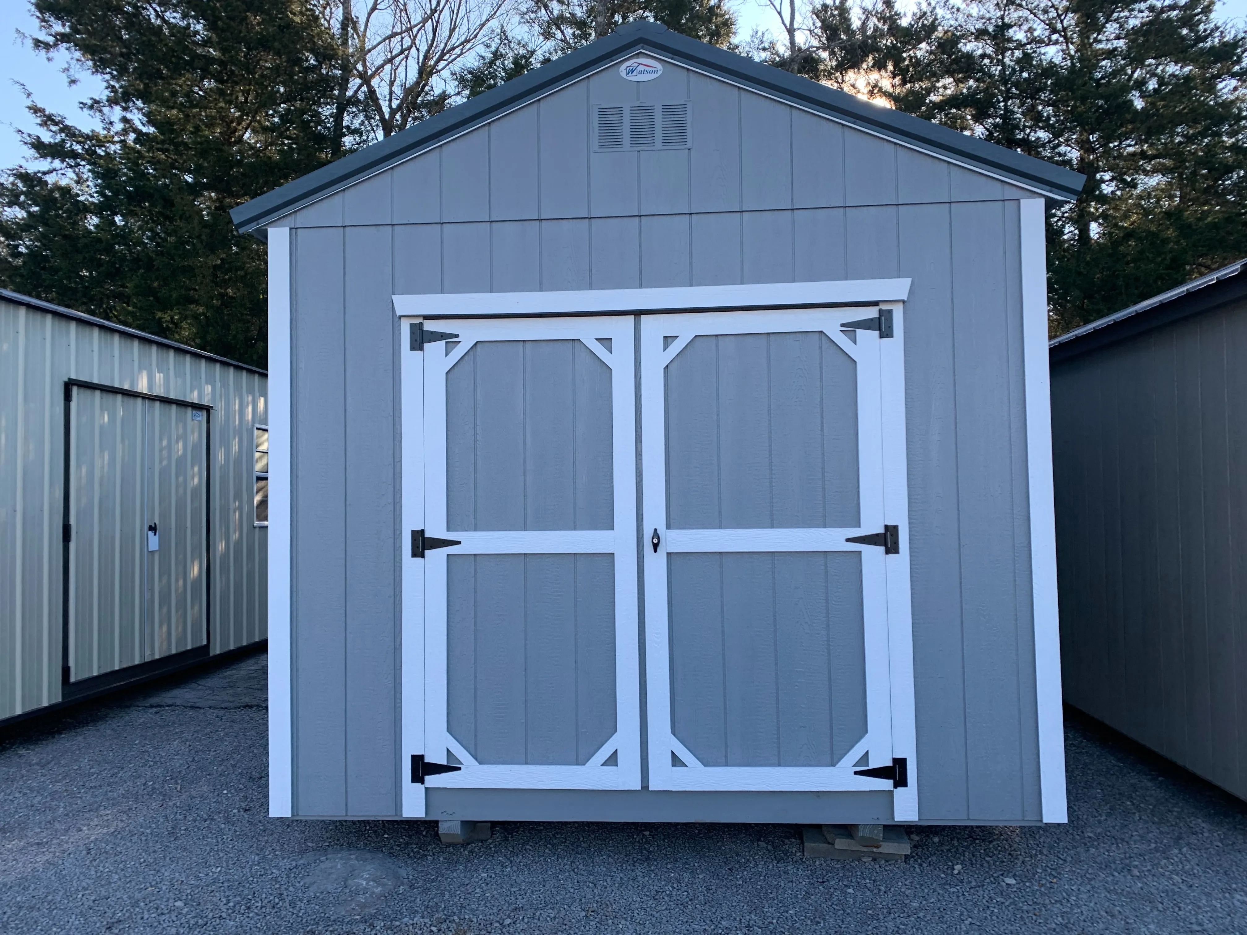 A light gray wood utility shed with white trim and double doors