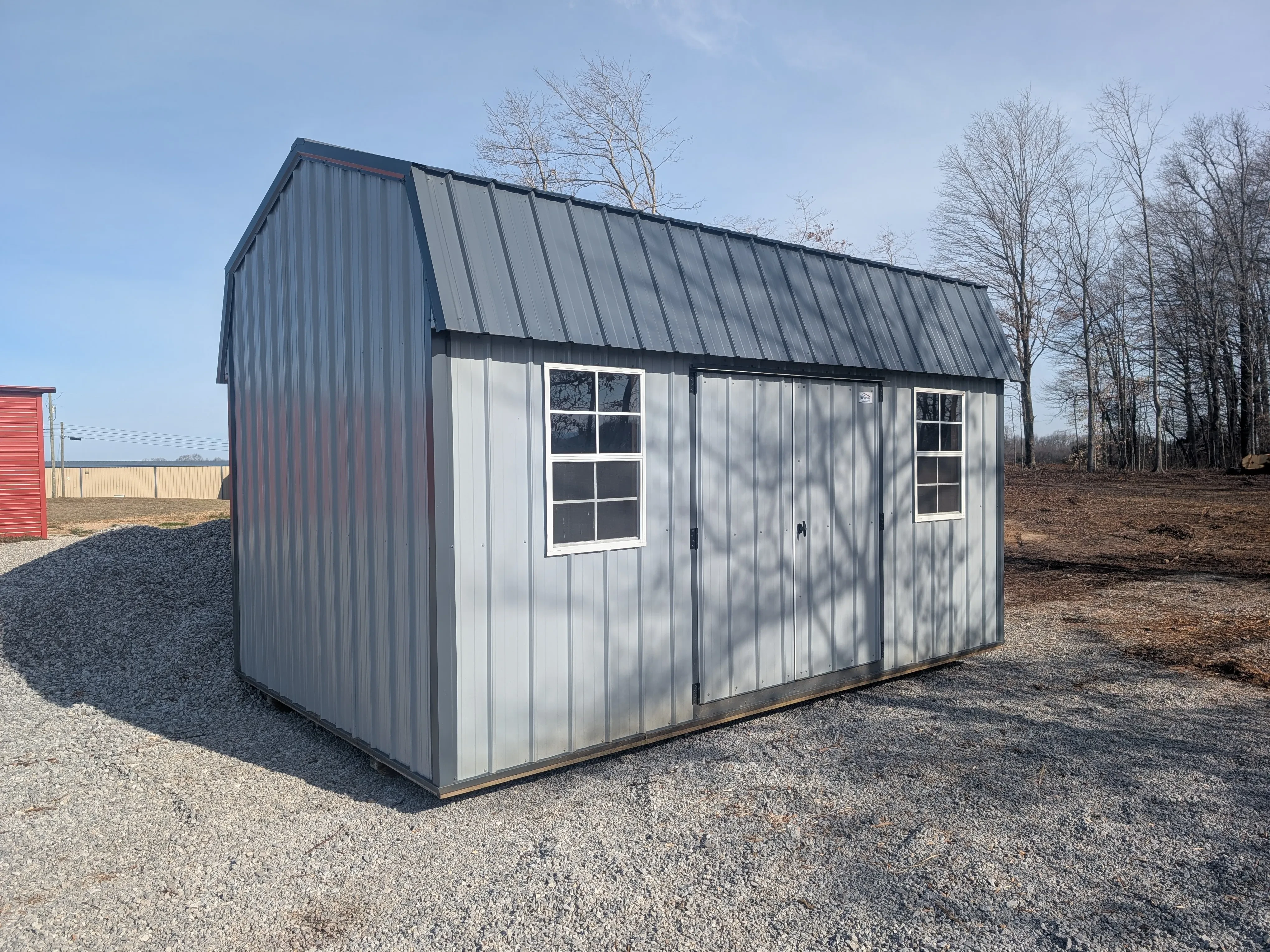 a metal side lofted barn. It has double doors and a 2x3 window on each side of the double doors. It is light gray