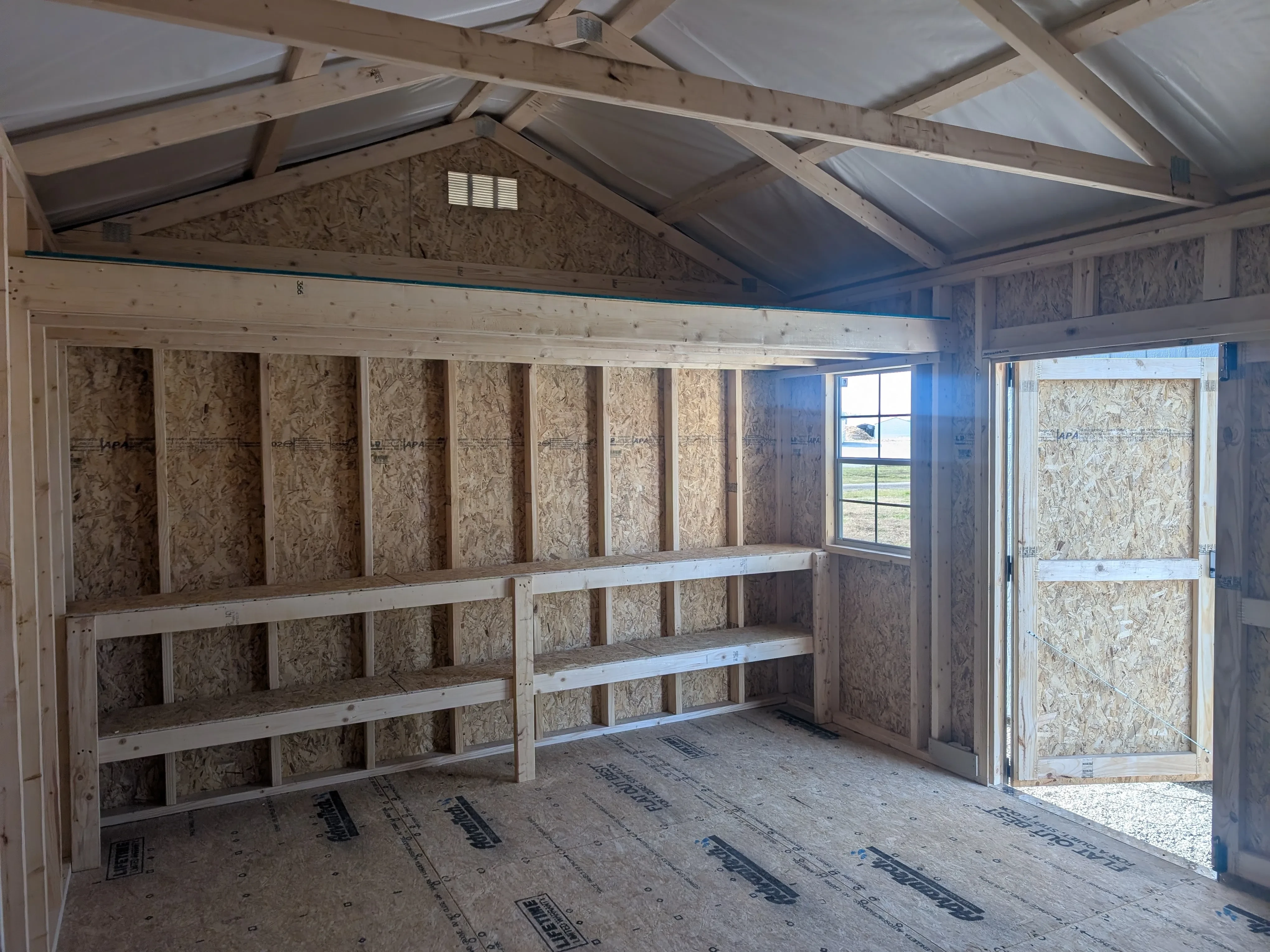 inside a wood garden shed. The right wall has double shelves and a loft up above. It has a vent near the roof