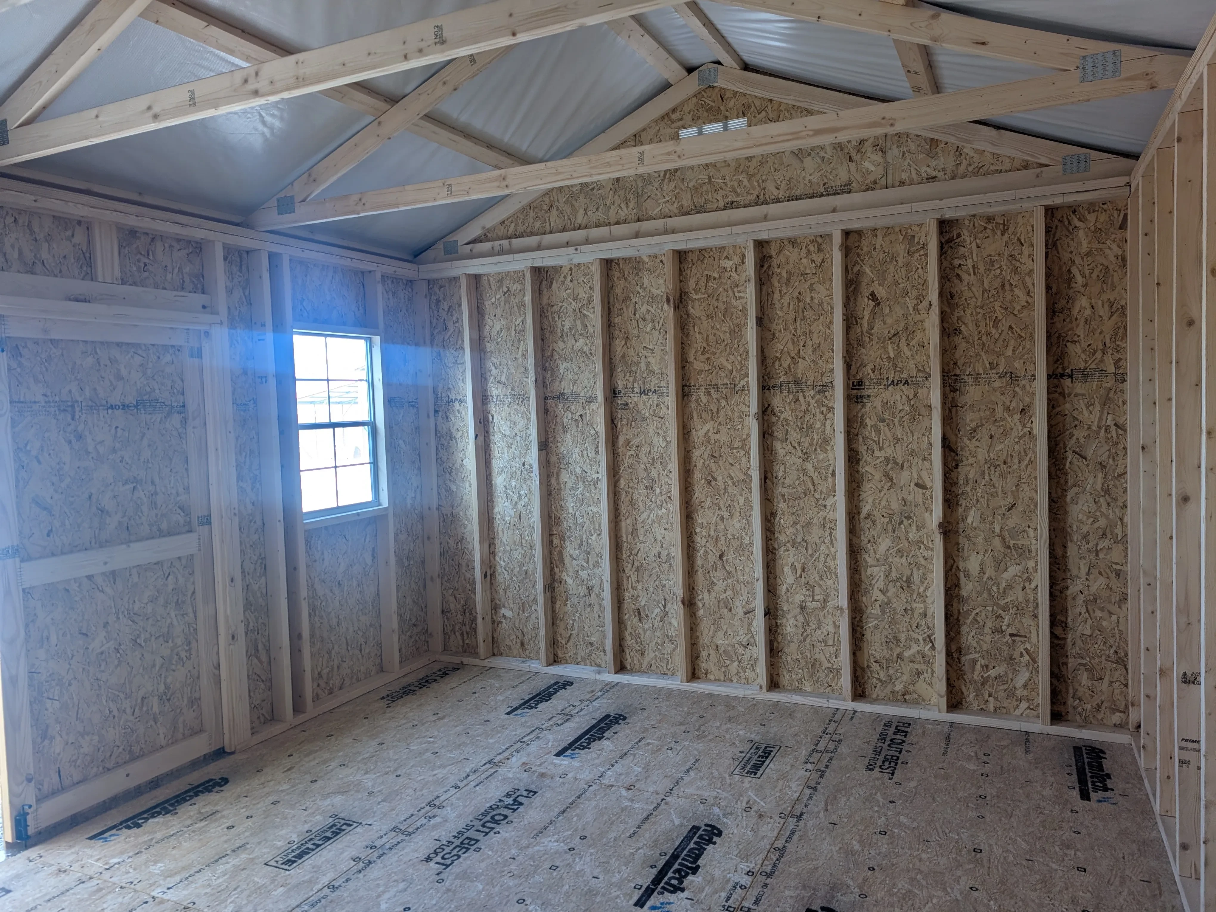 inside a wood garden shed looking at the left wall. The front wall has a window with light coming in and double doors