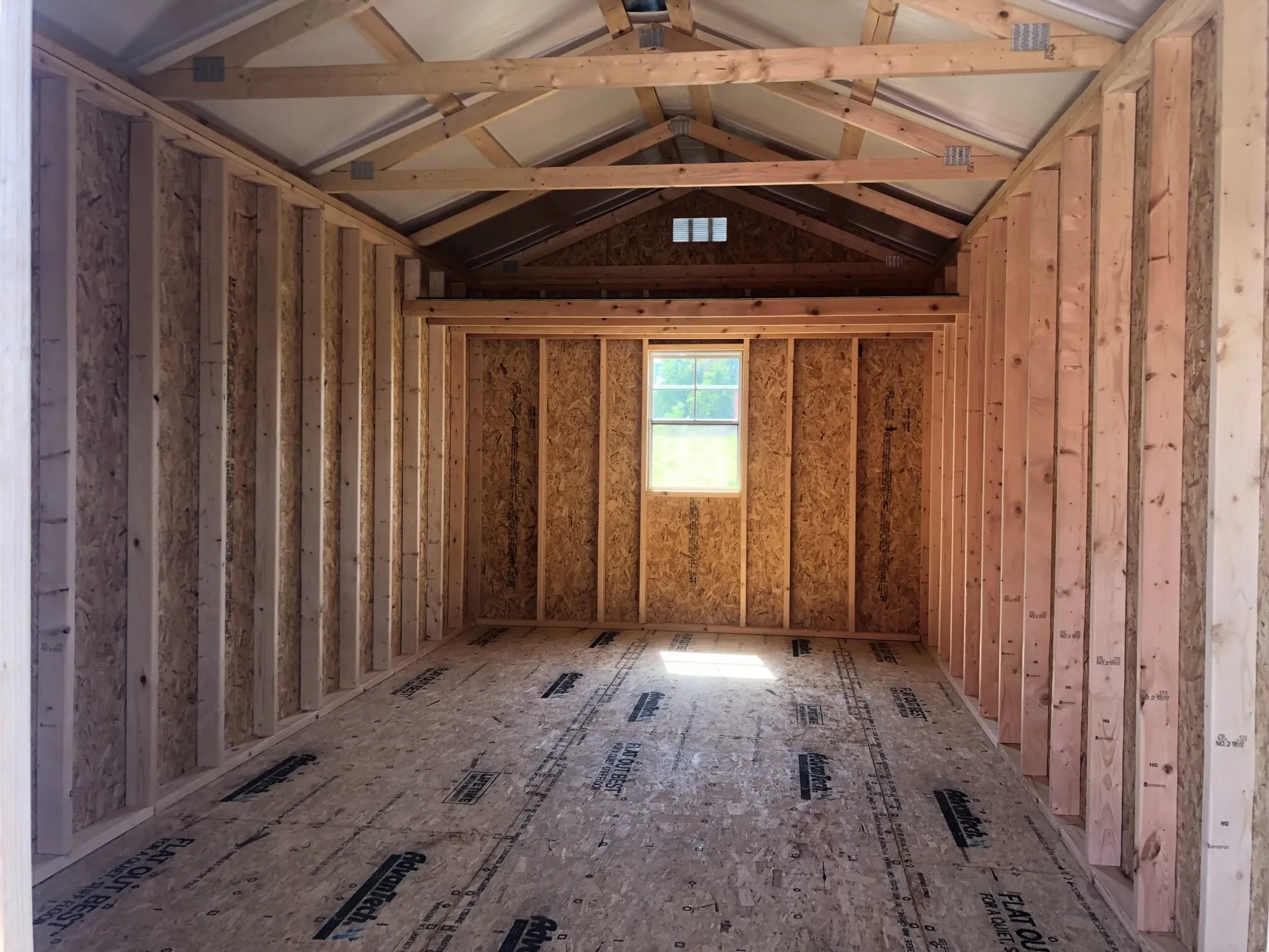 The inside of a wood shed showing a window in the middle of the back wall and a loft