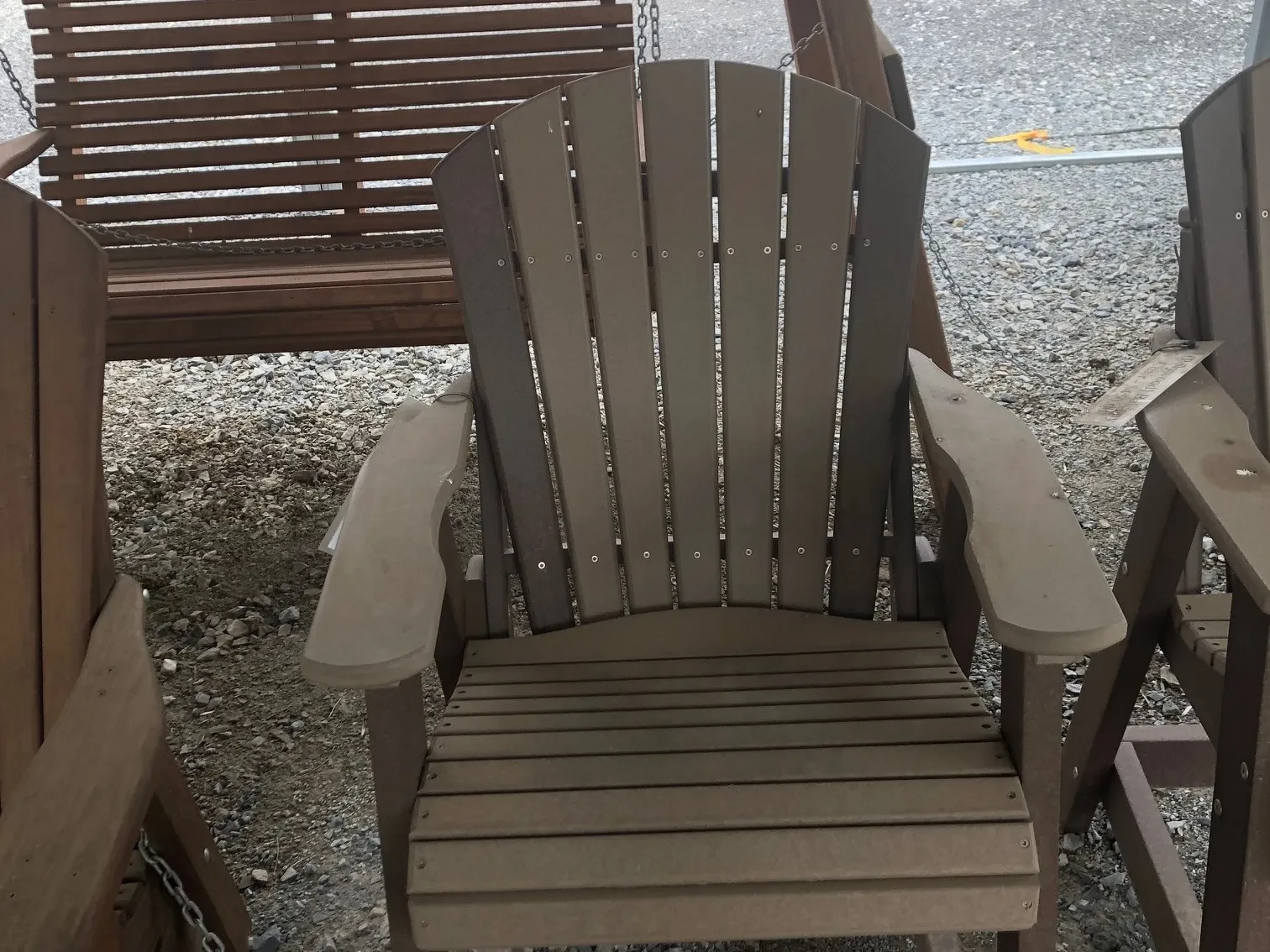 a chair sitting in the gravel. It has arm rests and foot rests. It is light gray with dark gray accents