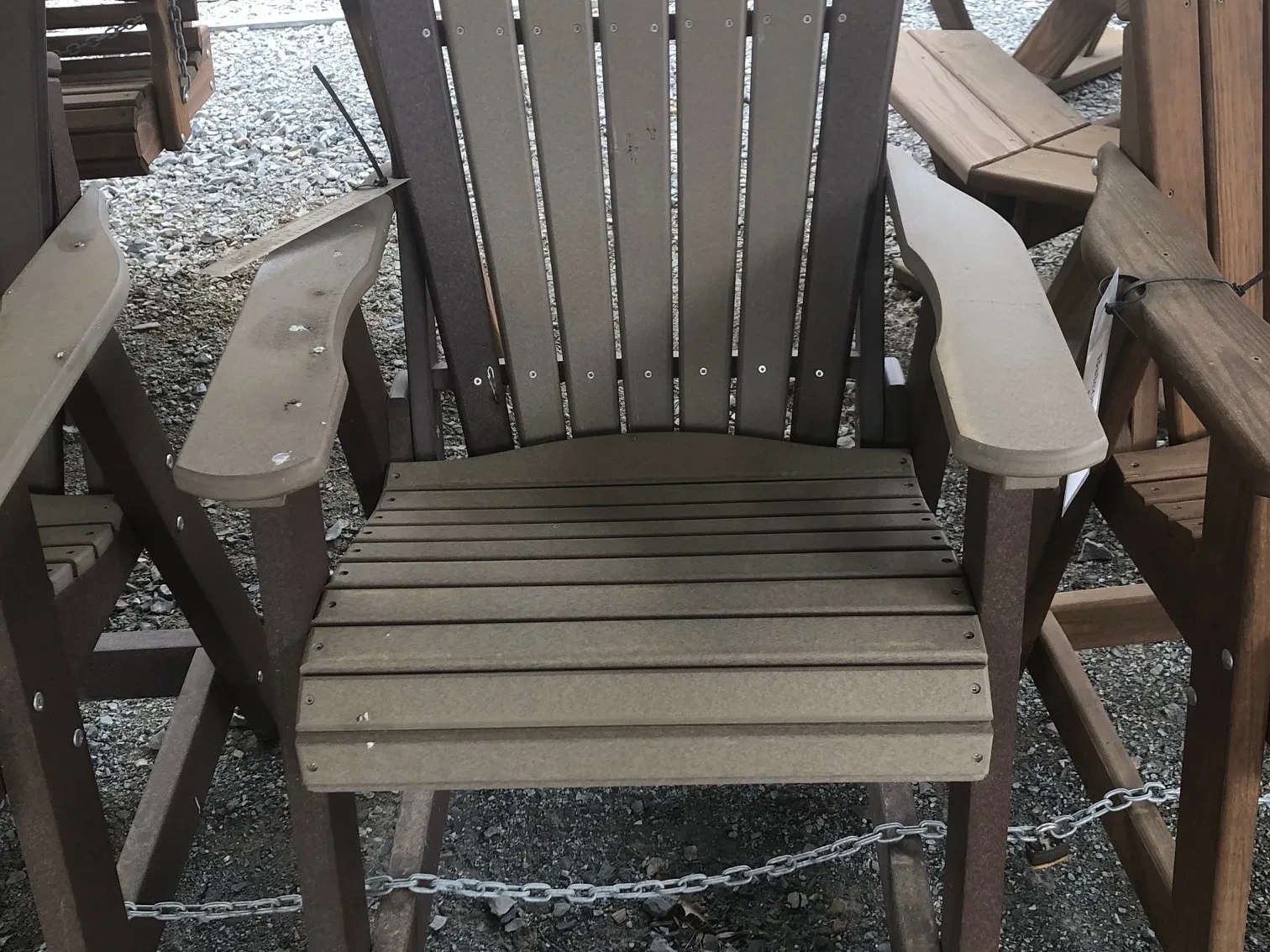 a light gray chair sitting in the gravel. It has dark gray accents. It is made out of a polywood material