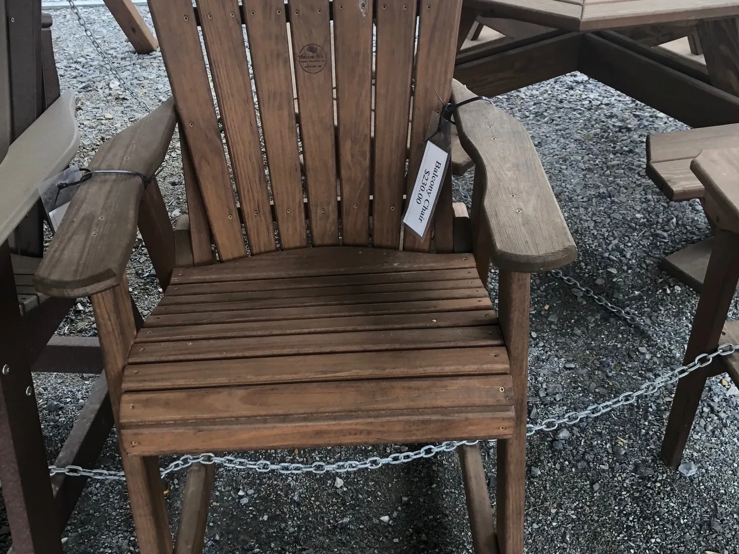 a wood stained and sealed chair with arm and foot rests. It is sitting in the gravel