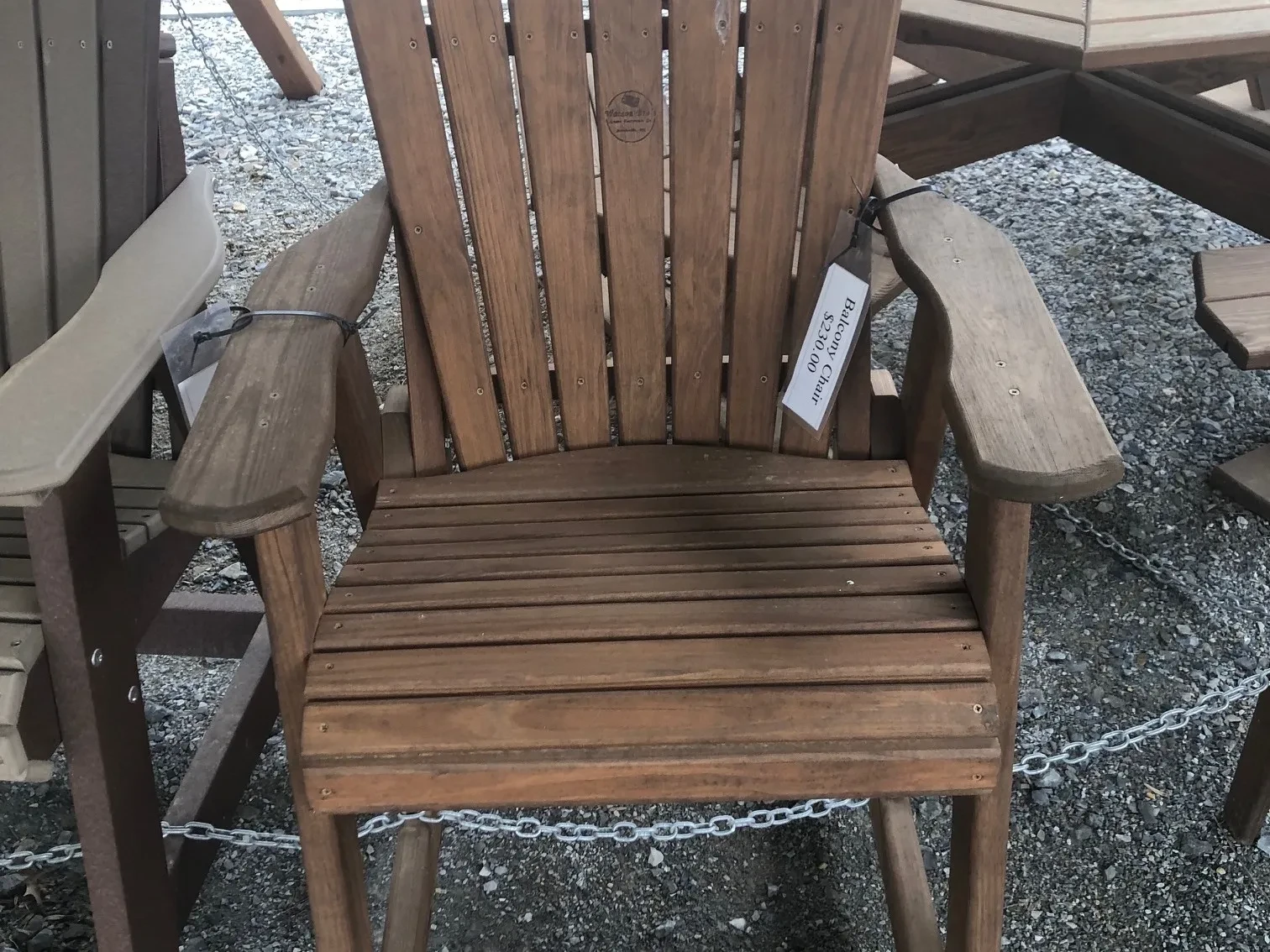 a chair sitting in the gravel. It is stained and sealed and has armrests and footrests. It is chained to other furniture