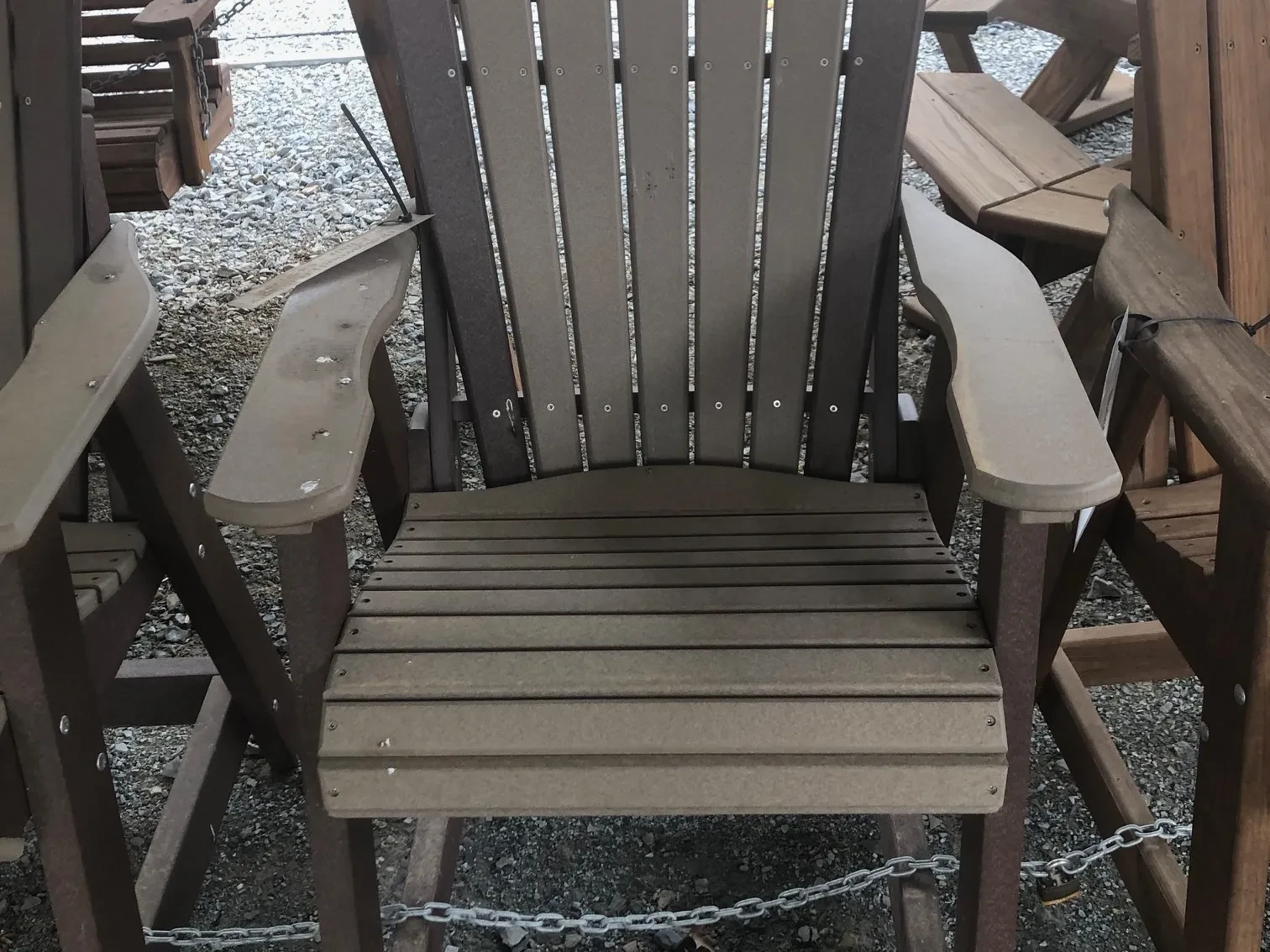 a chair made out of polywood sitting in the gravel. It is a light gray color and with dark gray accents