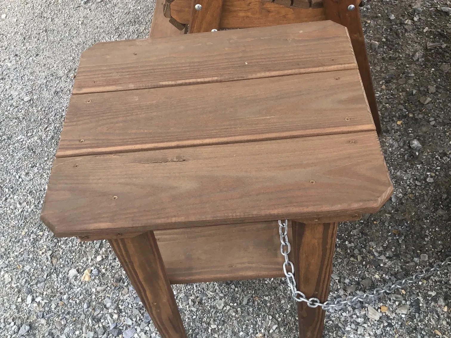 a wood stained and sealed table sitting in the gravel.