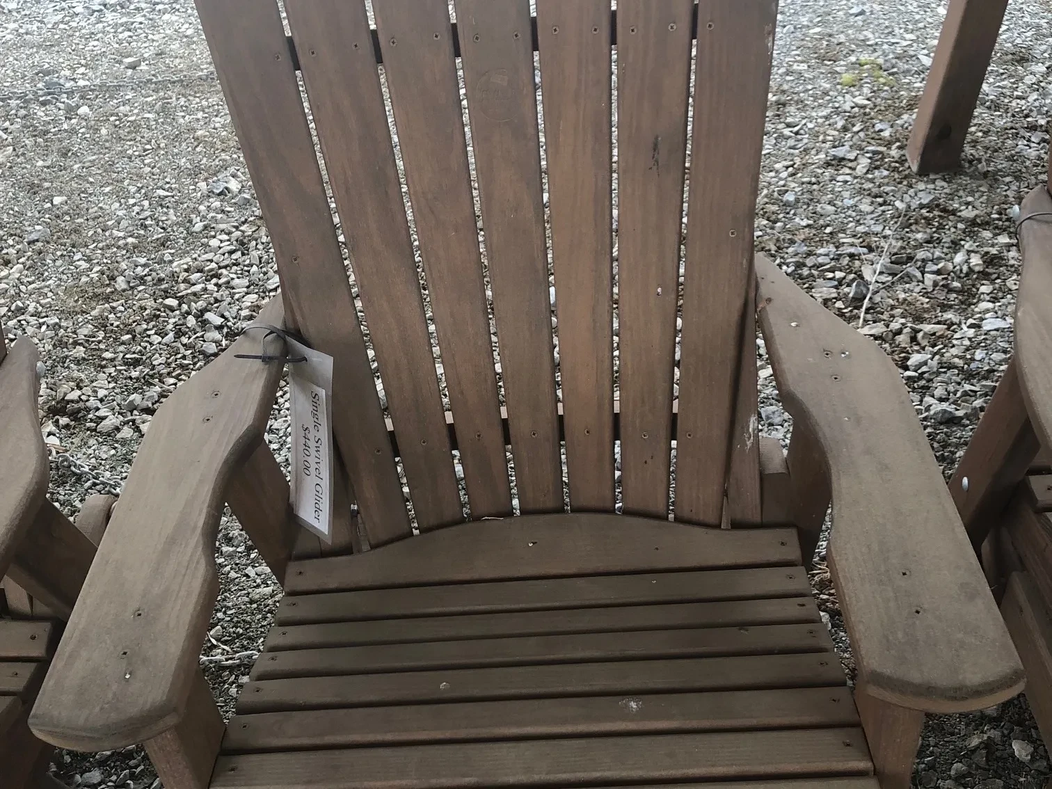 a stained and sealed wood chair sitting in the gravel. It can swivel 360° and glide back and forth