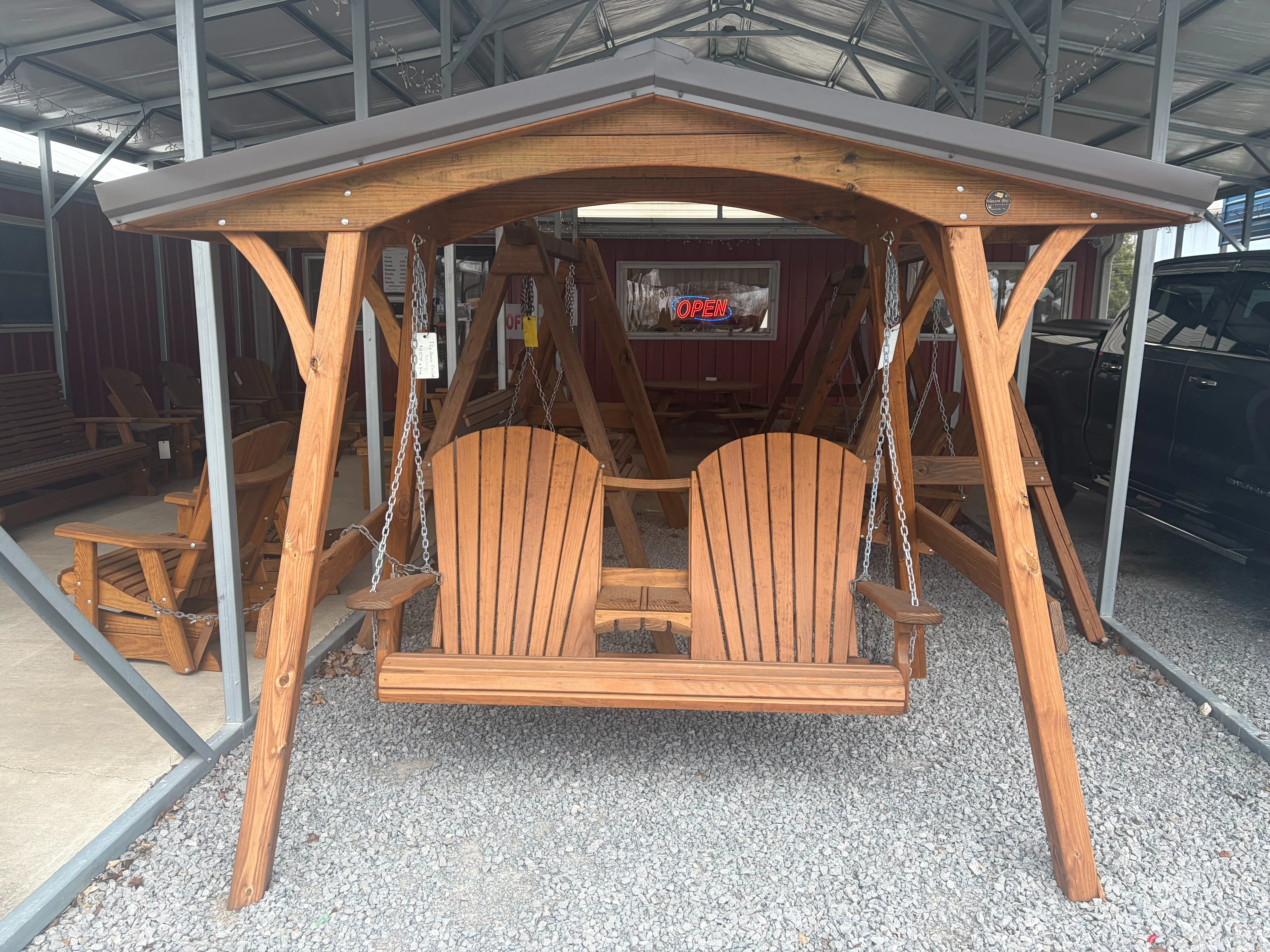 a wood a-frame structure with a metal roof on top. It is holding up a wooden swing bench. It is in the gravel