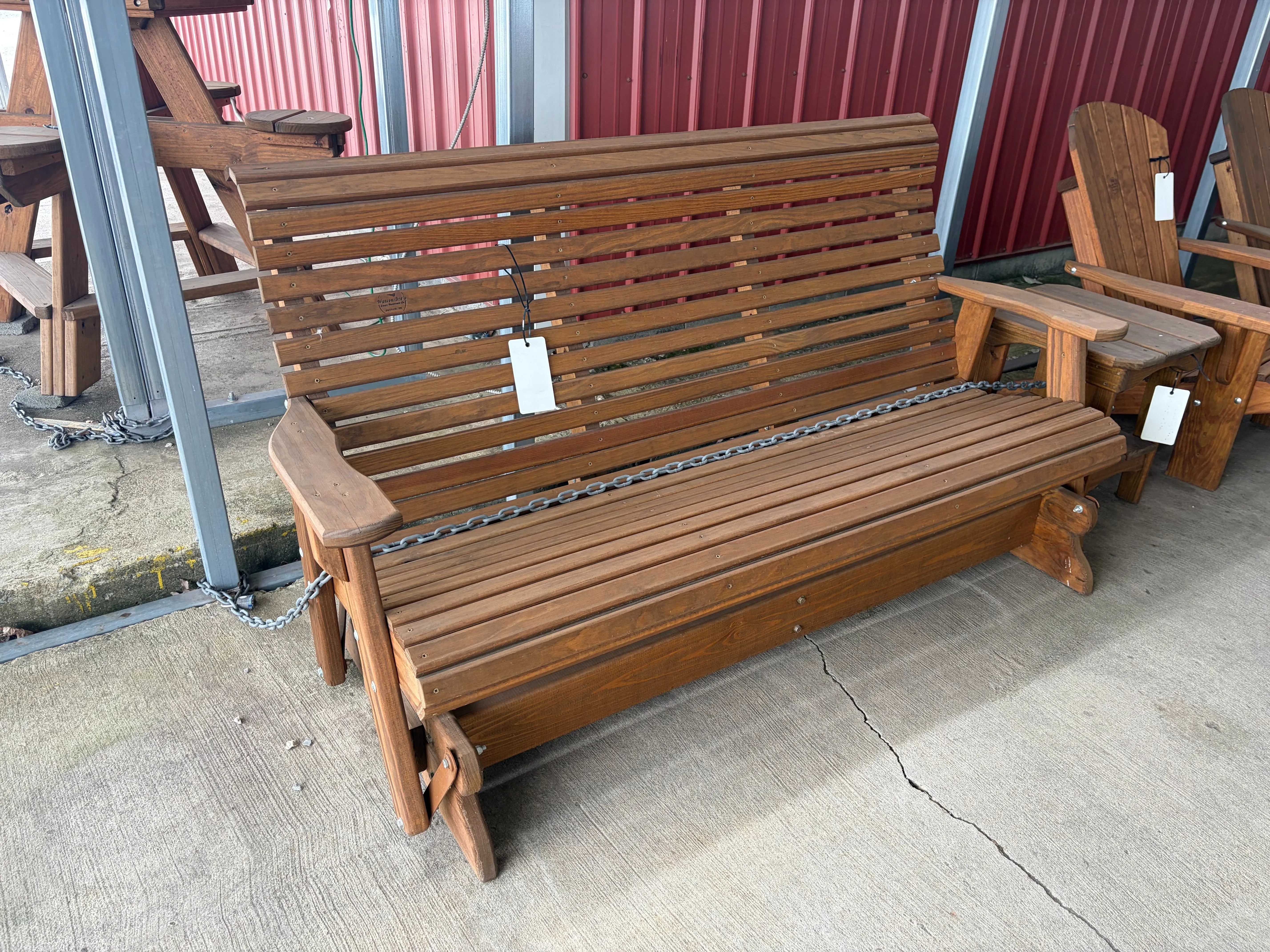 a bench sitting on concrete. It glides back and forth. It is stained and sealed. It has a price tag on the front of it