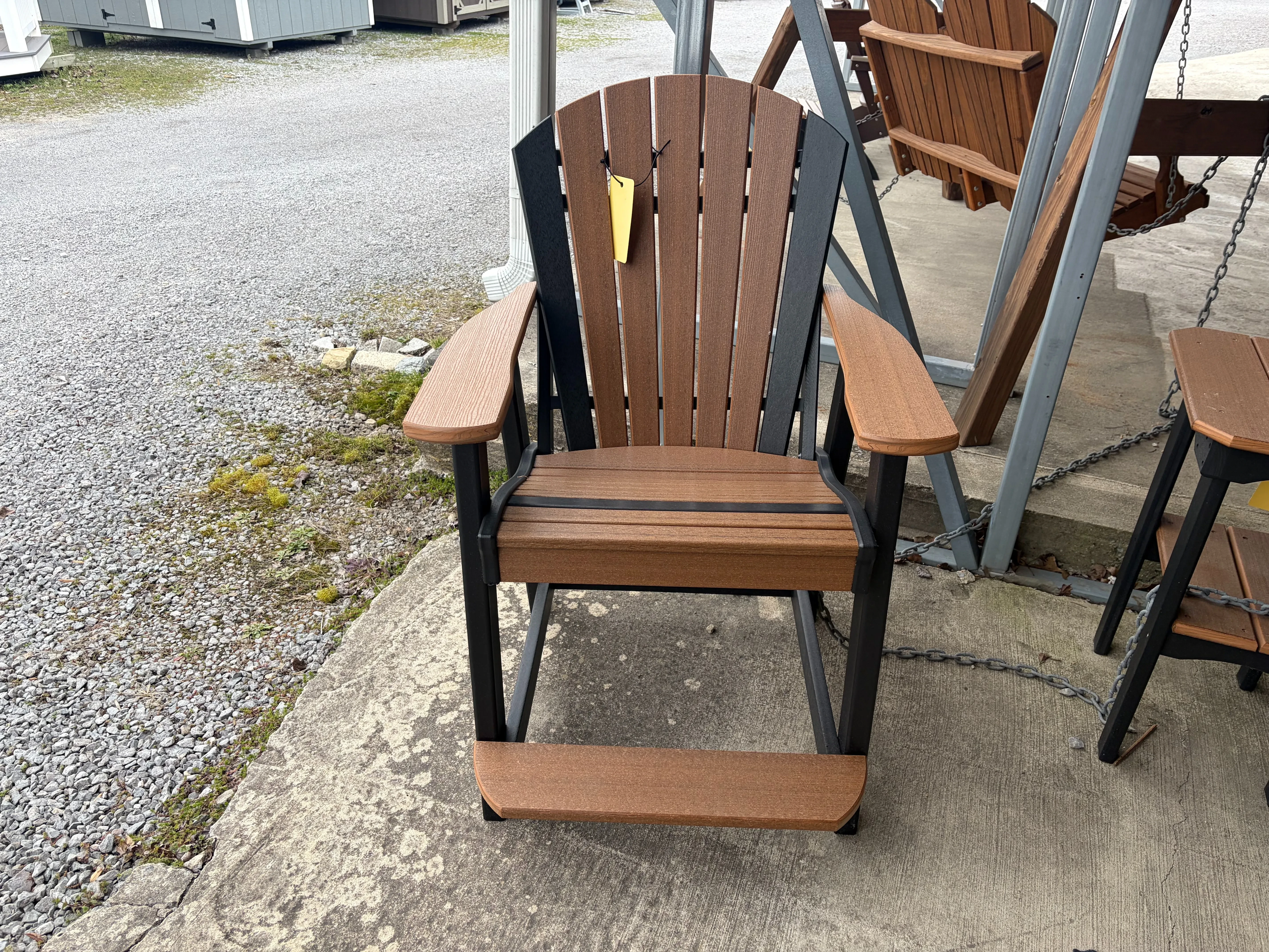 a brown chair with black accents sitting on concrete. It has a yellow price tag. It is made out of a polywood material