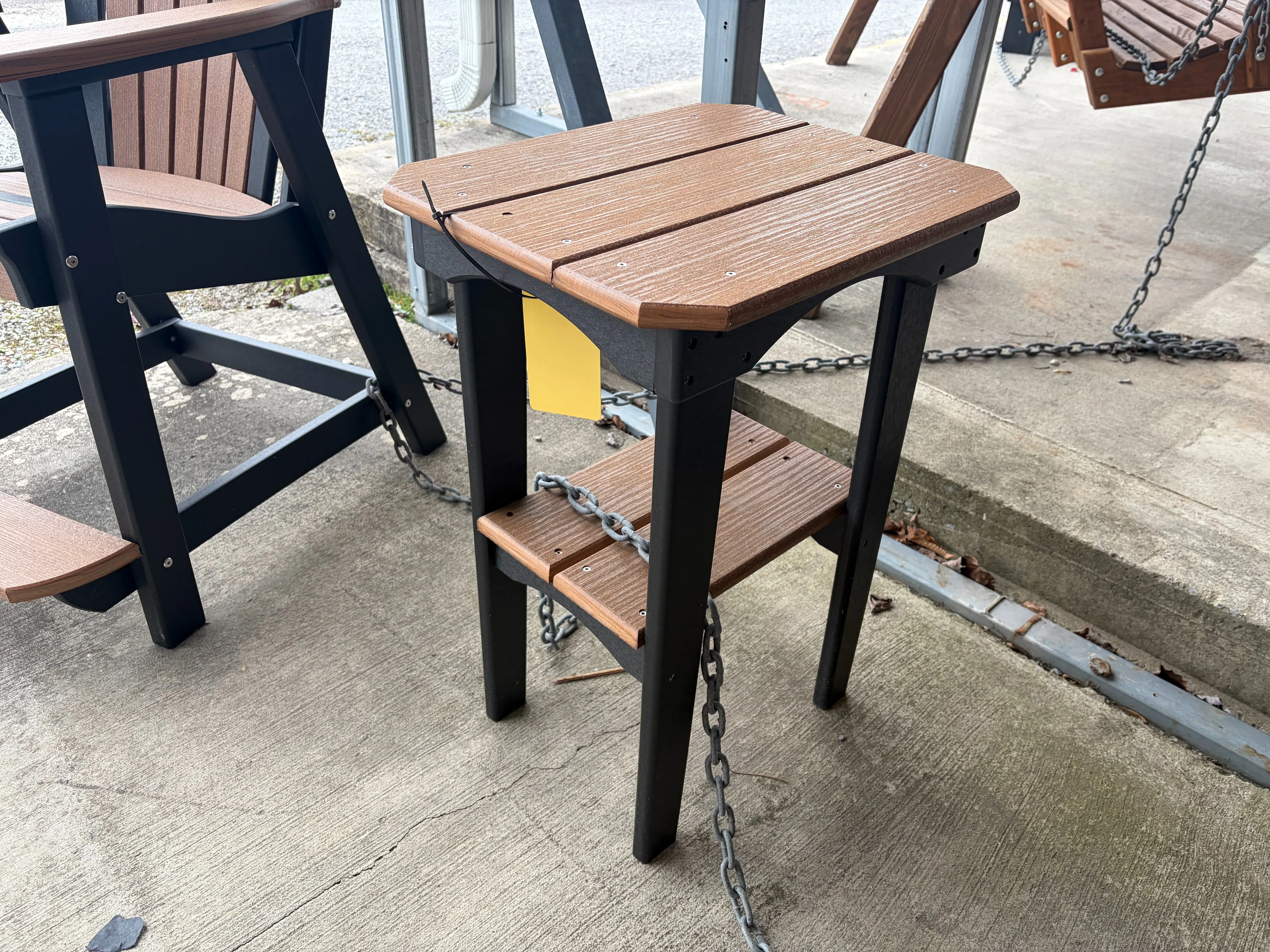 a table made out of polywood sitting on concrete. It has two brown tabletops and black legs. It is chained up to furniture