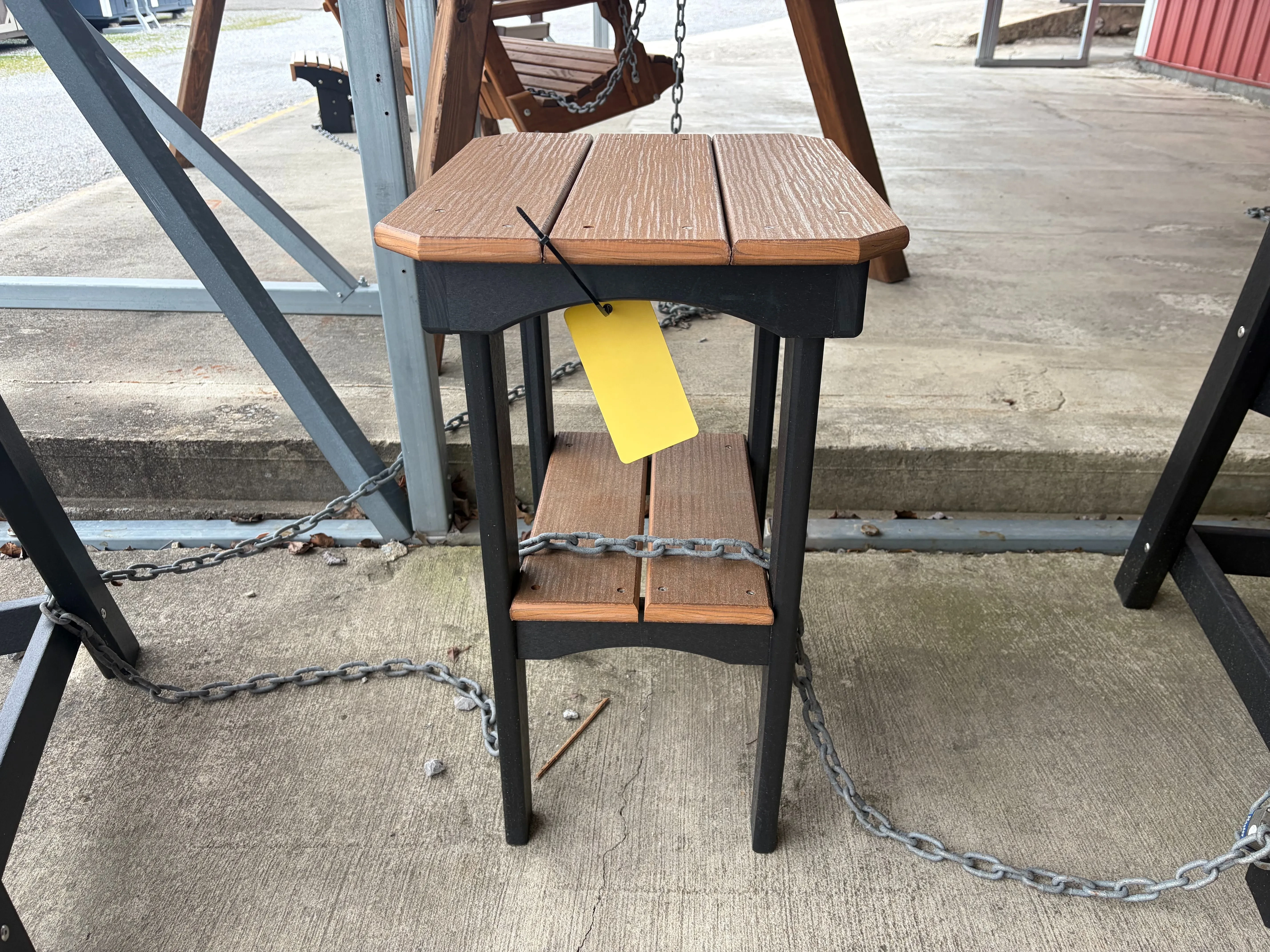 a brown table with black accents sitting on concrete. It has a yellow price tag and is chained up to other furniture