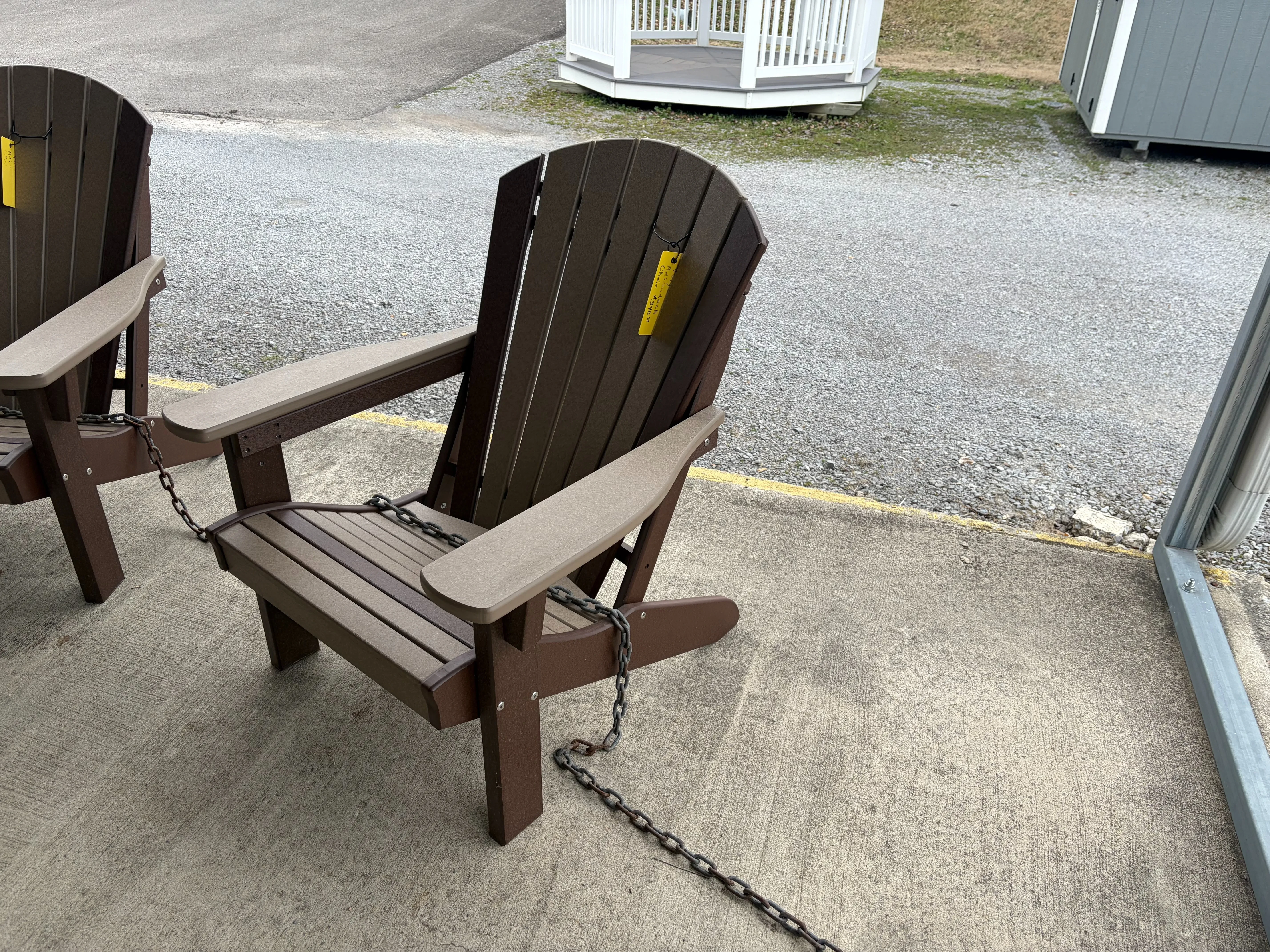 a chair made out of polywood sitting on concrete. It has armrests. It is brown with dark brown accents