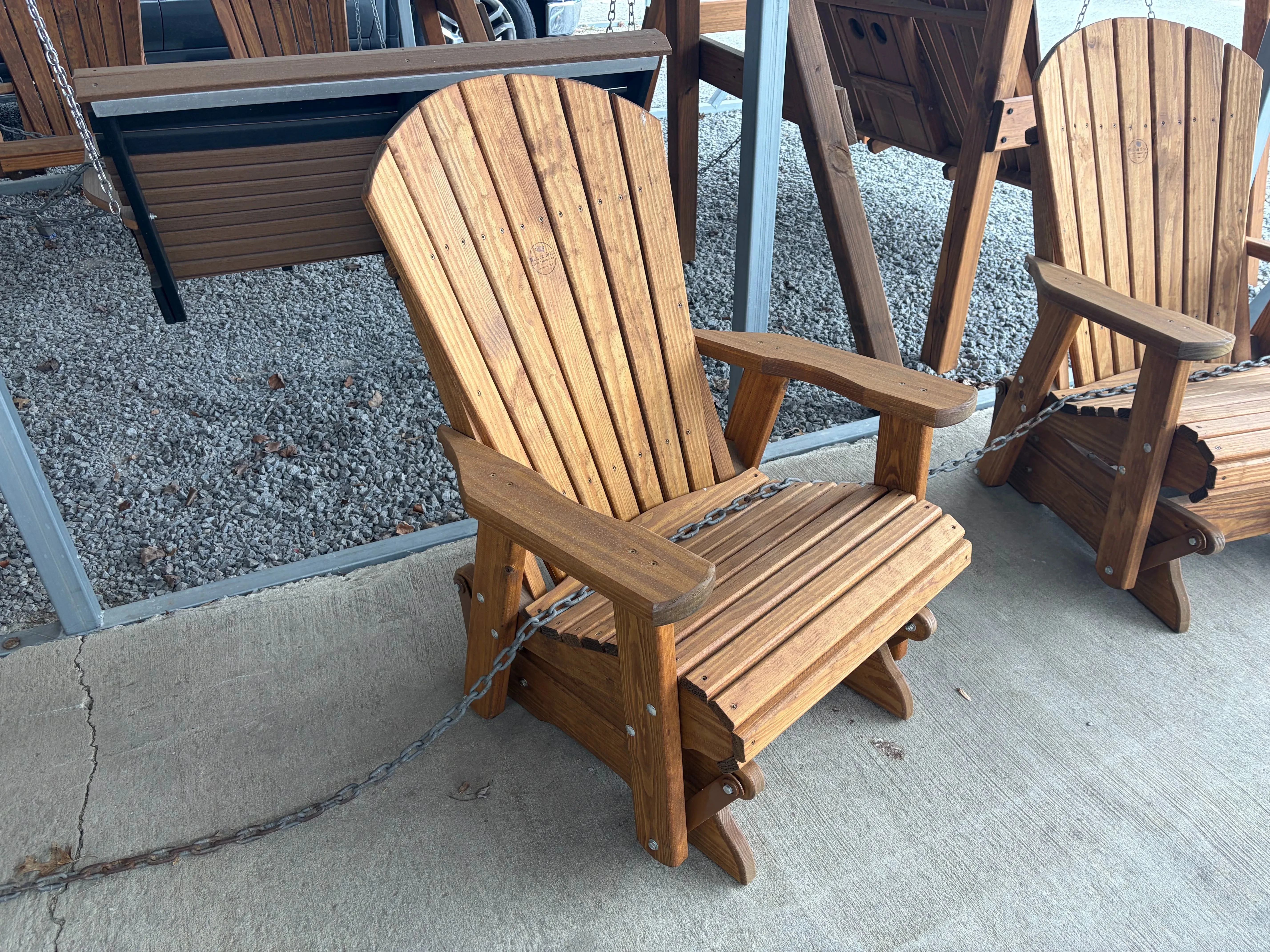a wood chair that has been stained and sealed sitting on concrete. It can glide back and forth. It is next to other chairs