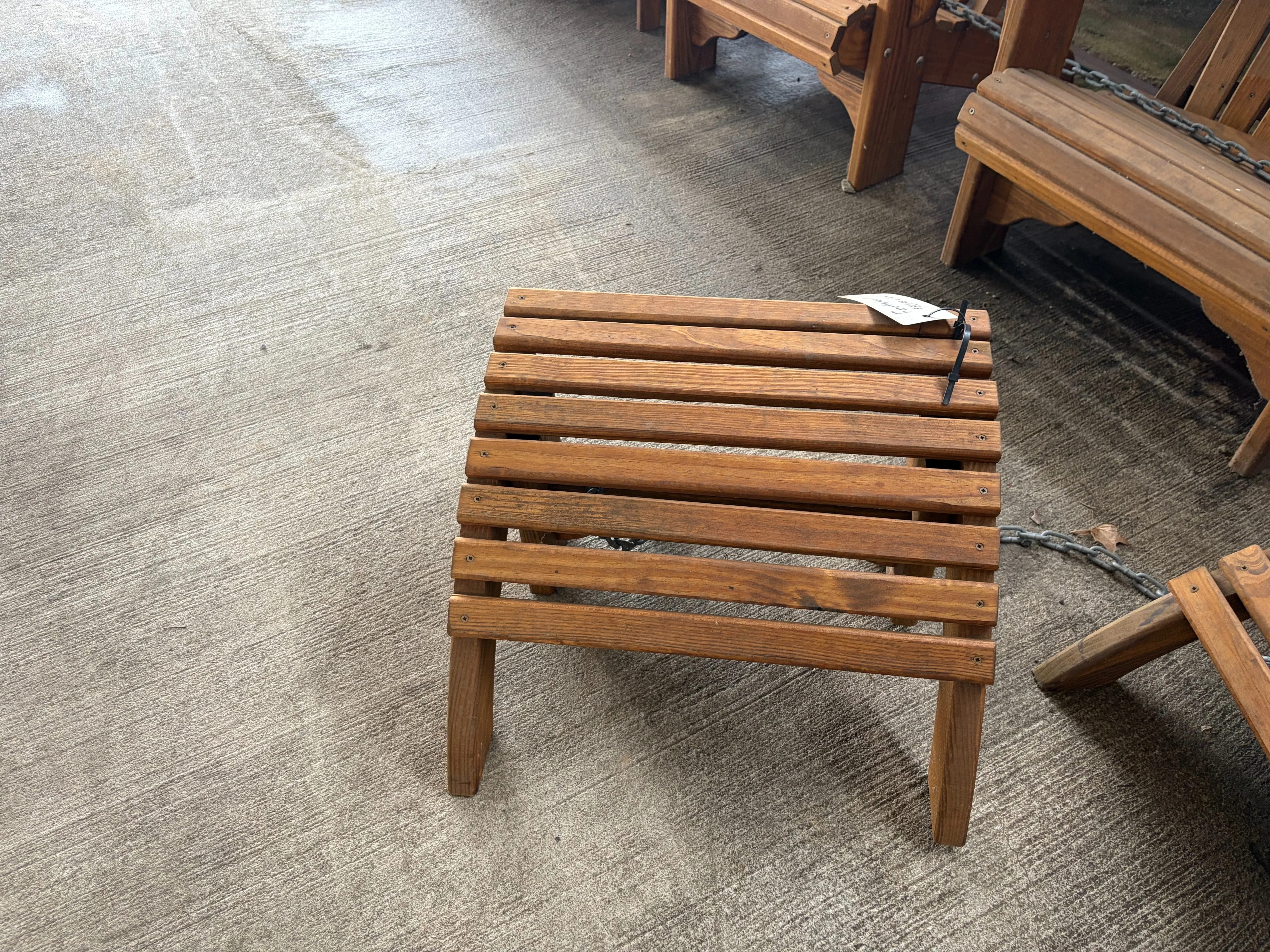 a wooden foot stool sitting on concrete. It has a white price tag on it