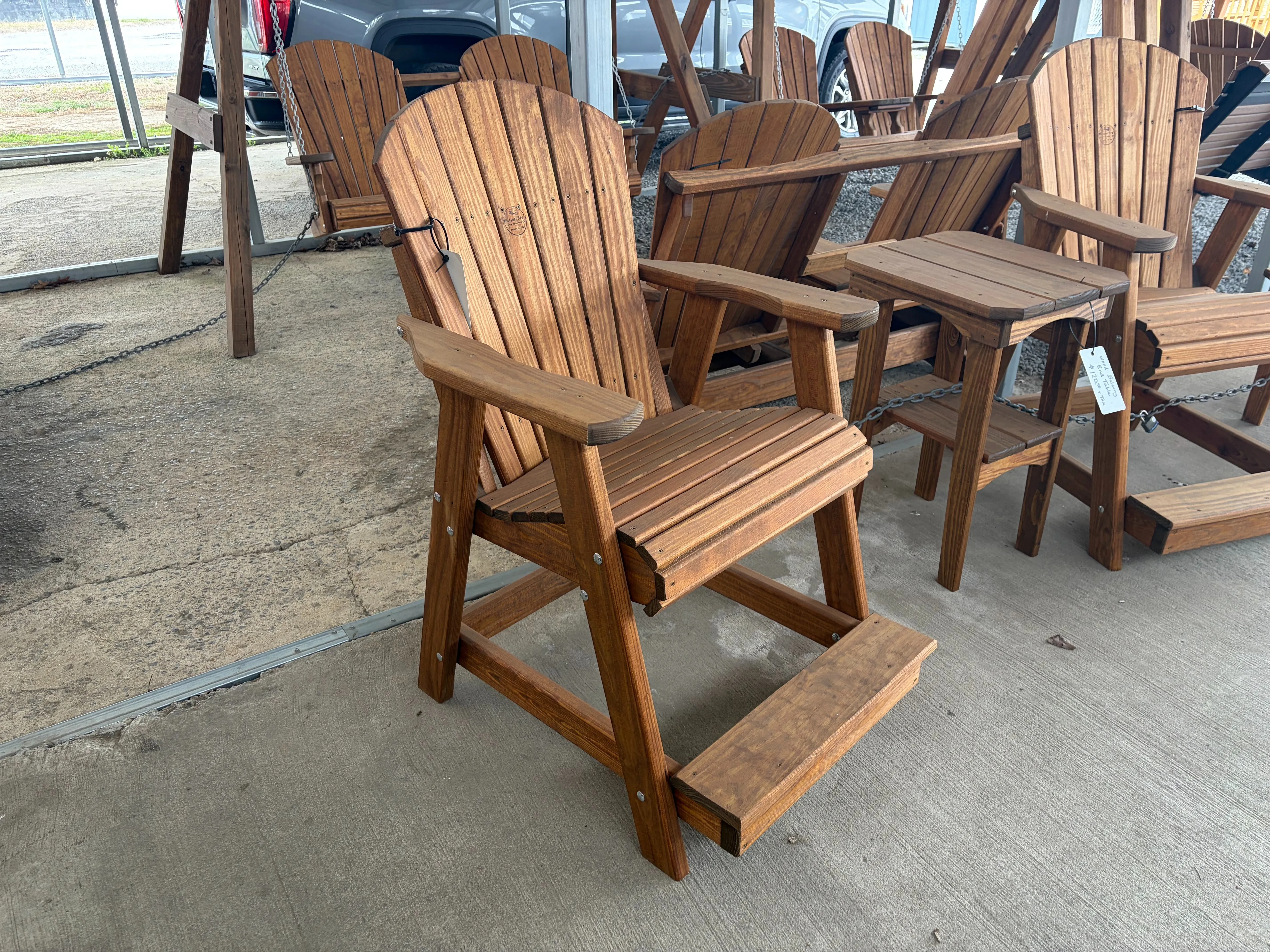 a wood chair sitting on concrete. It is stained and sealed. It is next to other furniture and has a white price tag on it