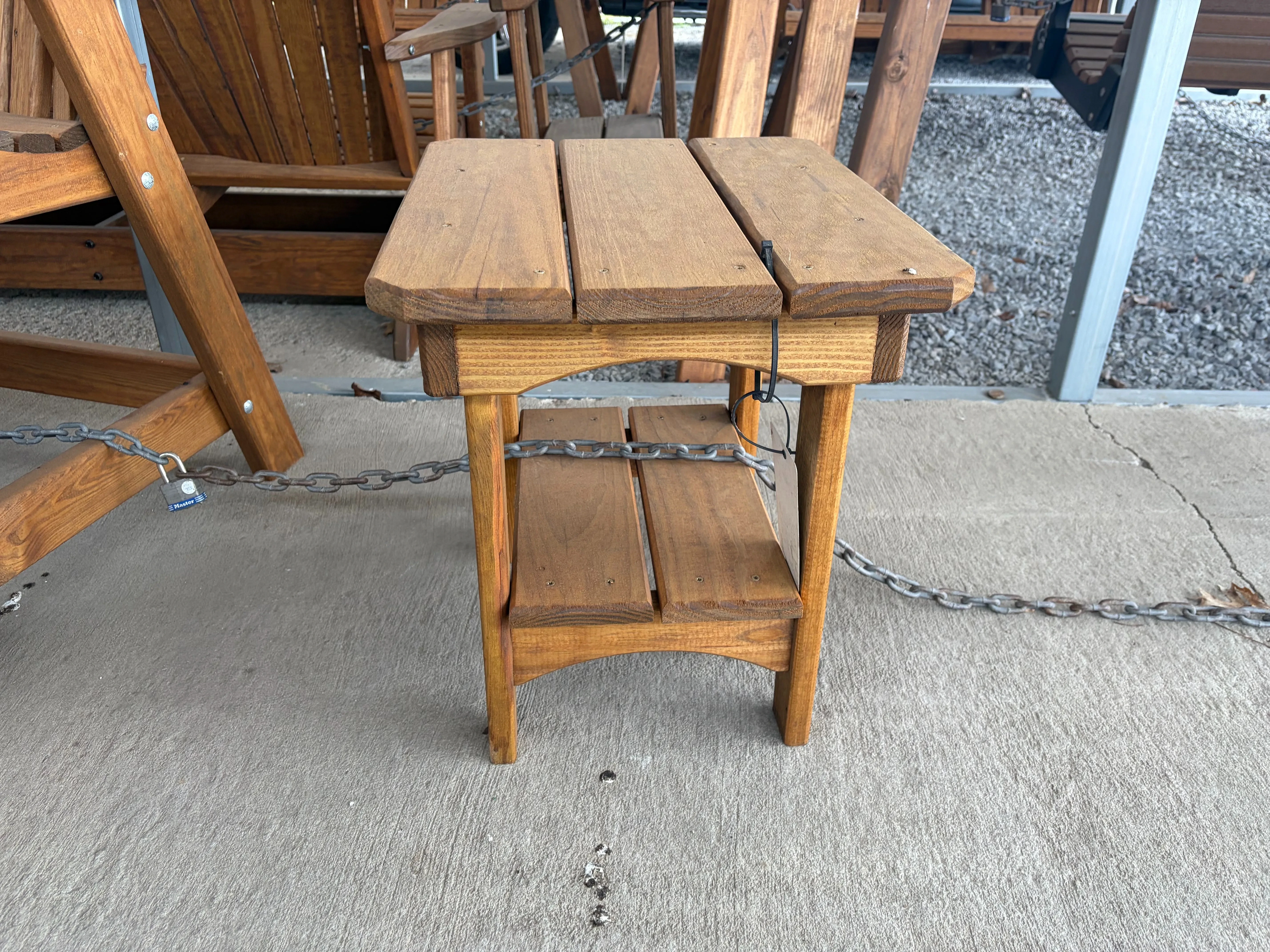 a wood stained and sealed table sitting on concrete. It is chained up to other furniture so nobody steals it