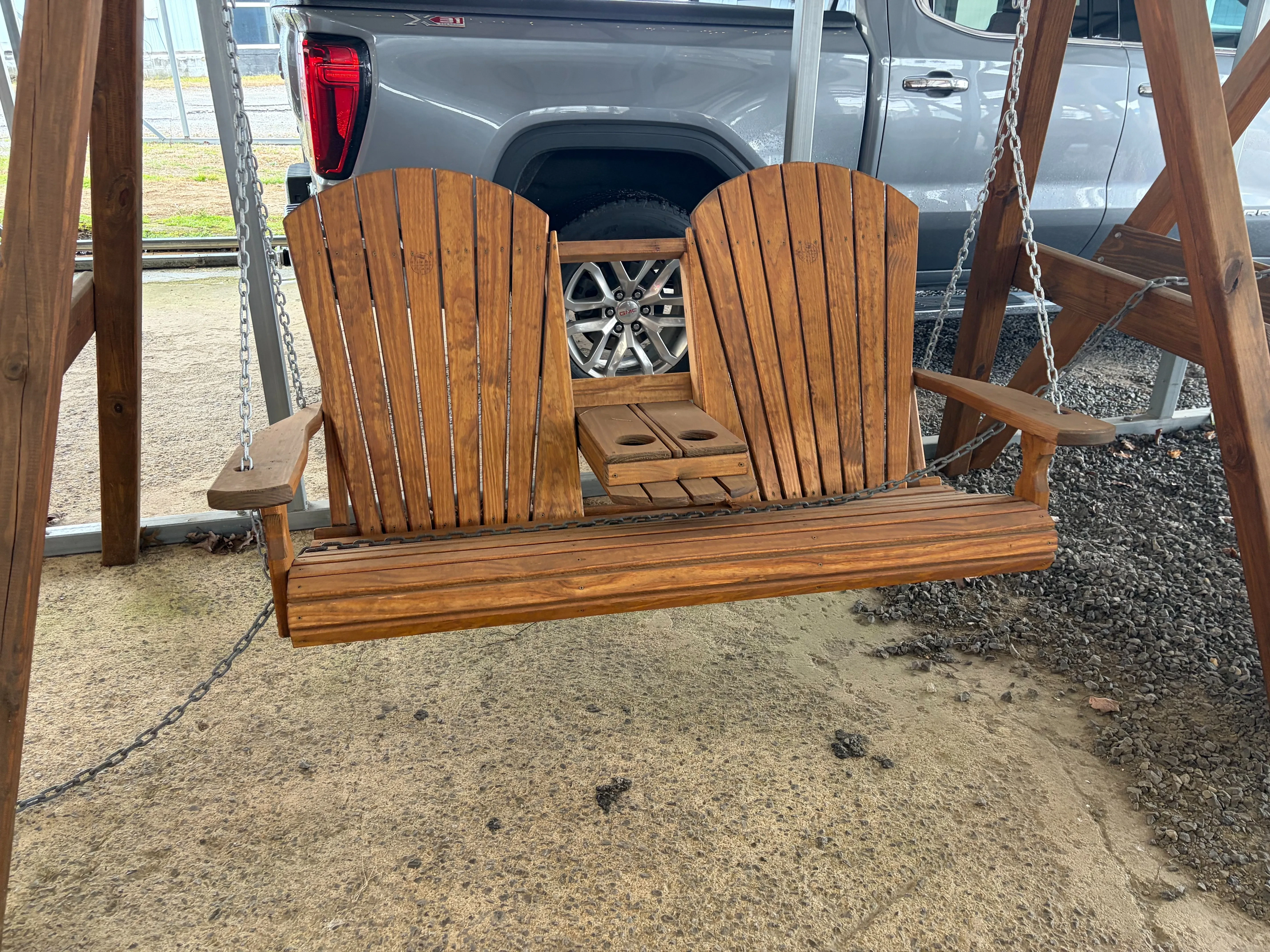 a wood swing bench held up by chains attached to a wooden a-frame structure. It has a center console in the down position