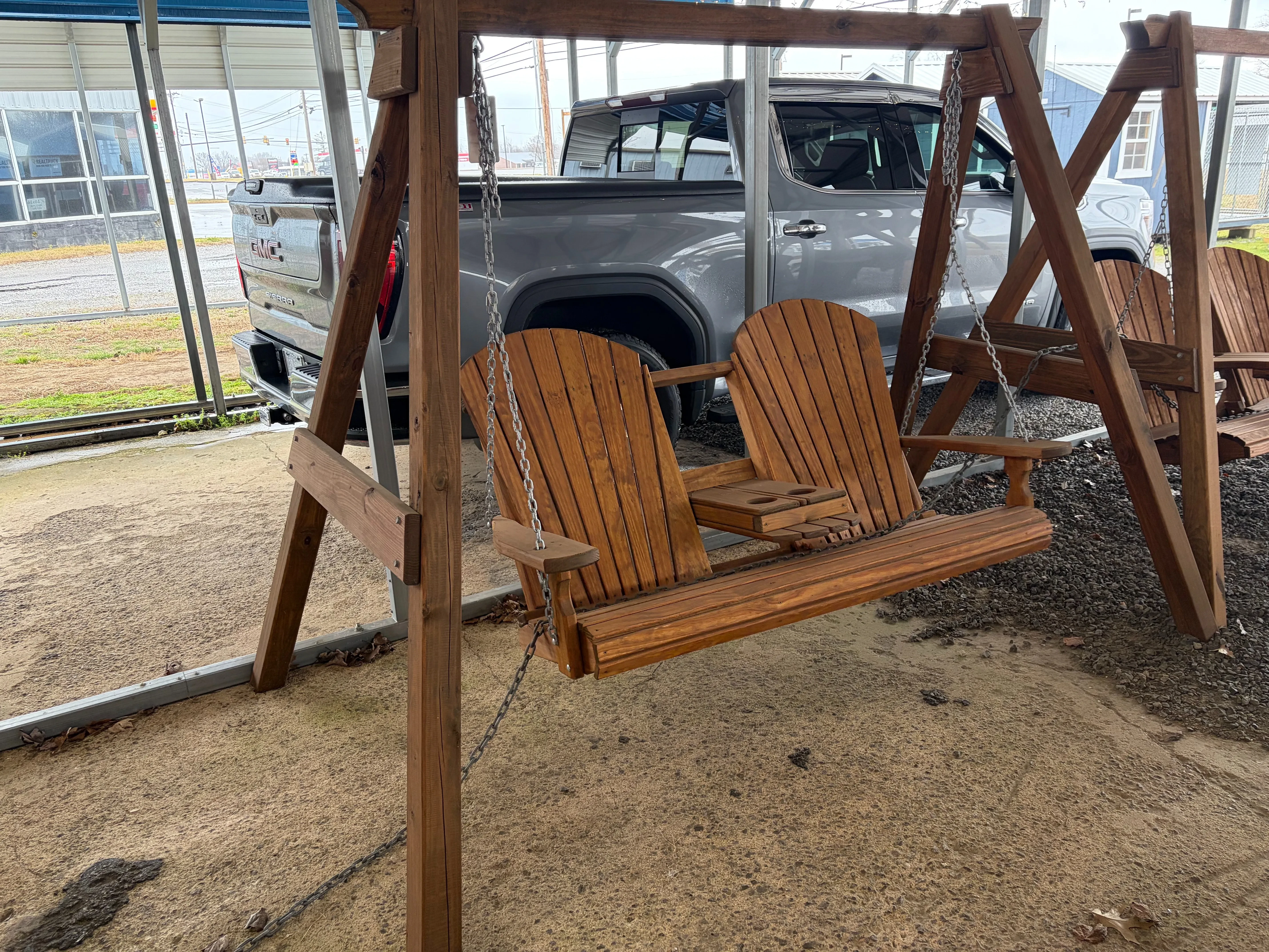 a wood stained and sealed swing bench hovering over concrete. It is attahced to a wood a-frame.