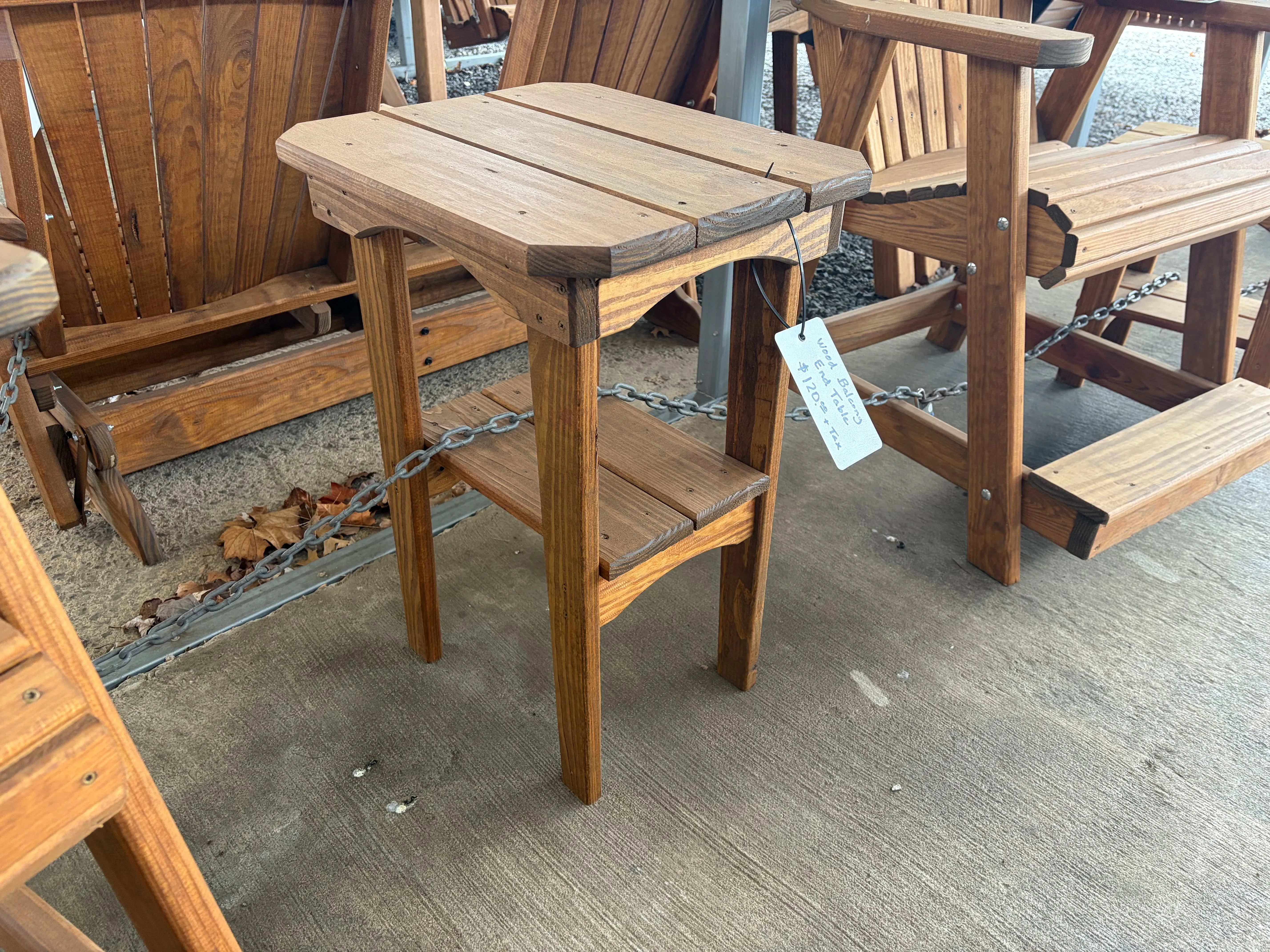 a stained and sealed table standing on concrete. It has a white price tag. It is chained up to other furniture nearby