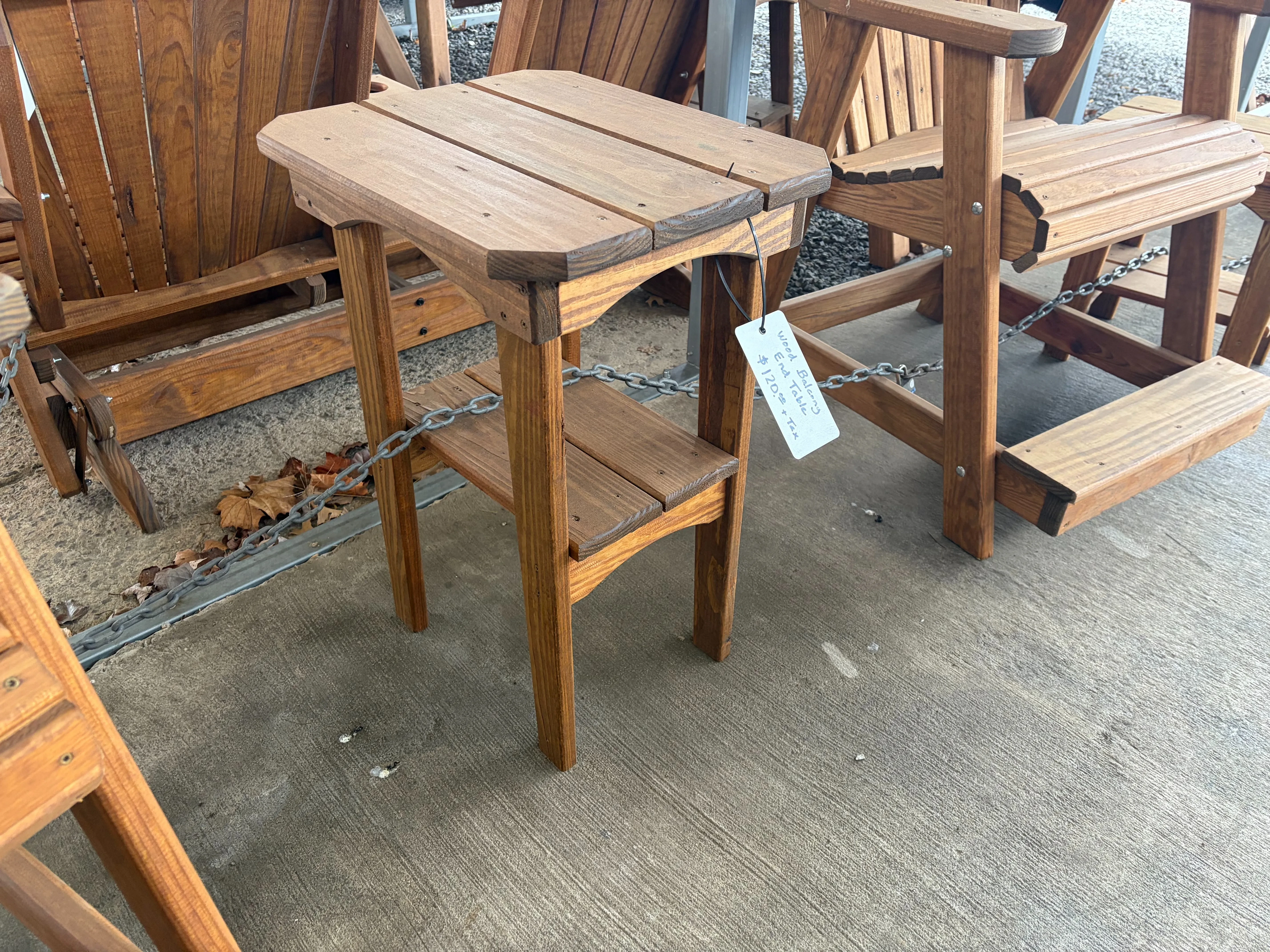 a table standing on concrete. It is stained and sealed. It has a white price tag hanging off and is chained to furniture