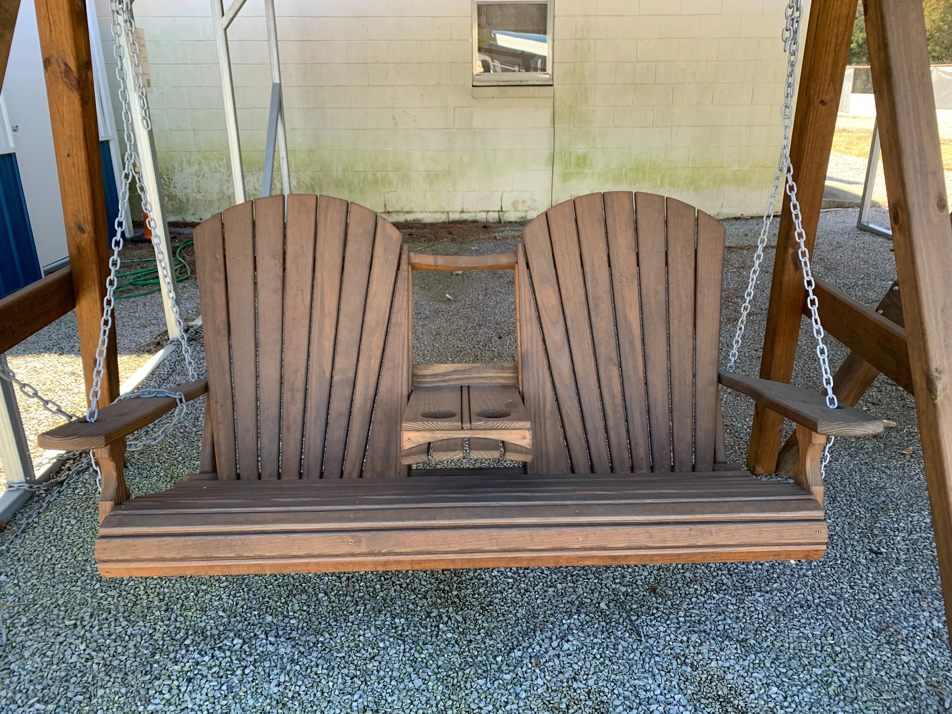 a wood stained and sealed bench swing hanging by chains attached the an a-frame structure. It has a center console